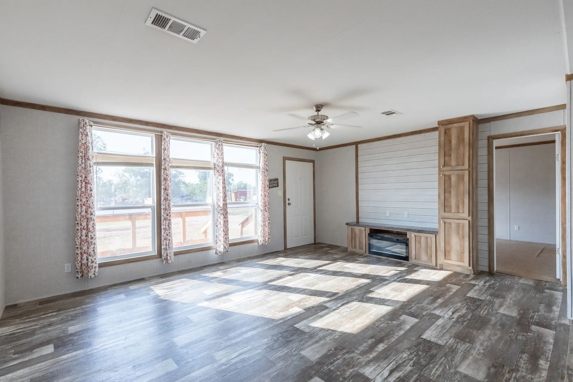 Open-concept living space with wood-finish flooring, a built-in entertainment center, and a ceiling fan