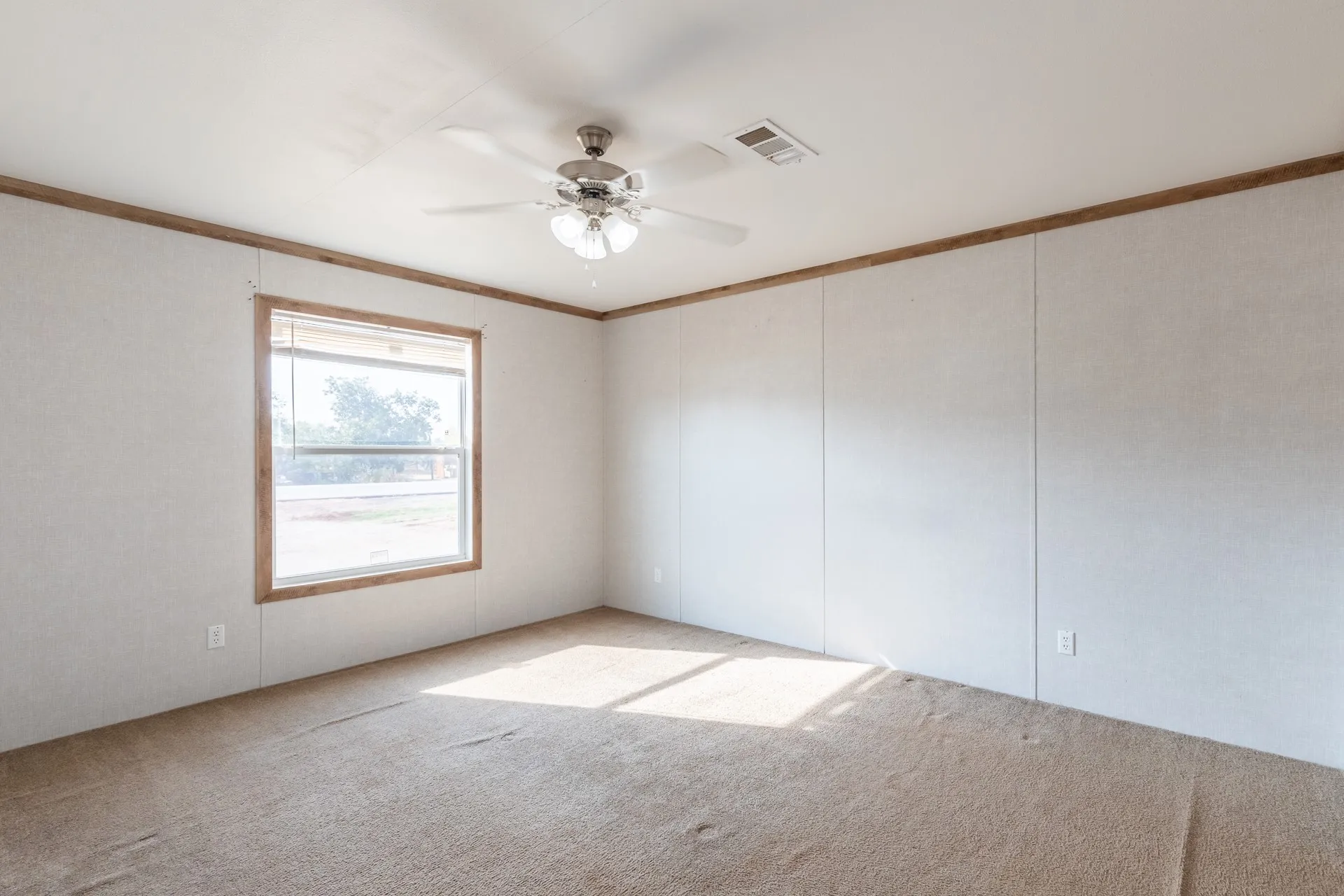 Neutral-toned carpeting, a ceiling fan with integrated lighting, and a single window with blinds