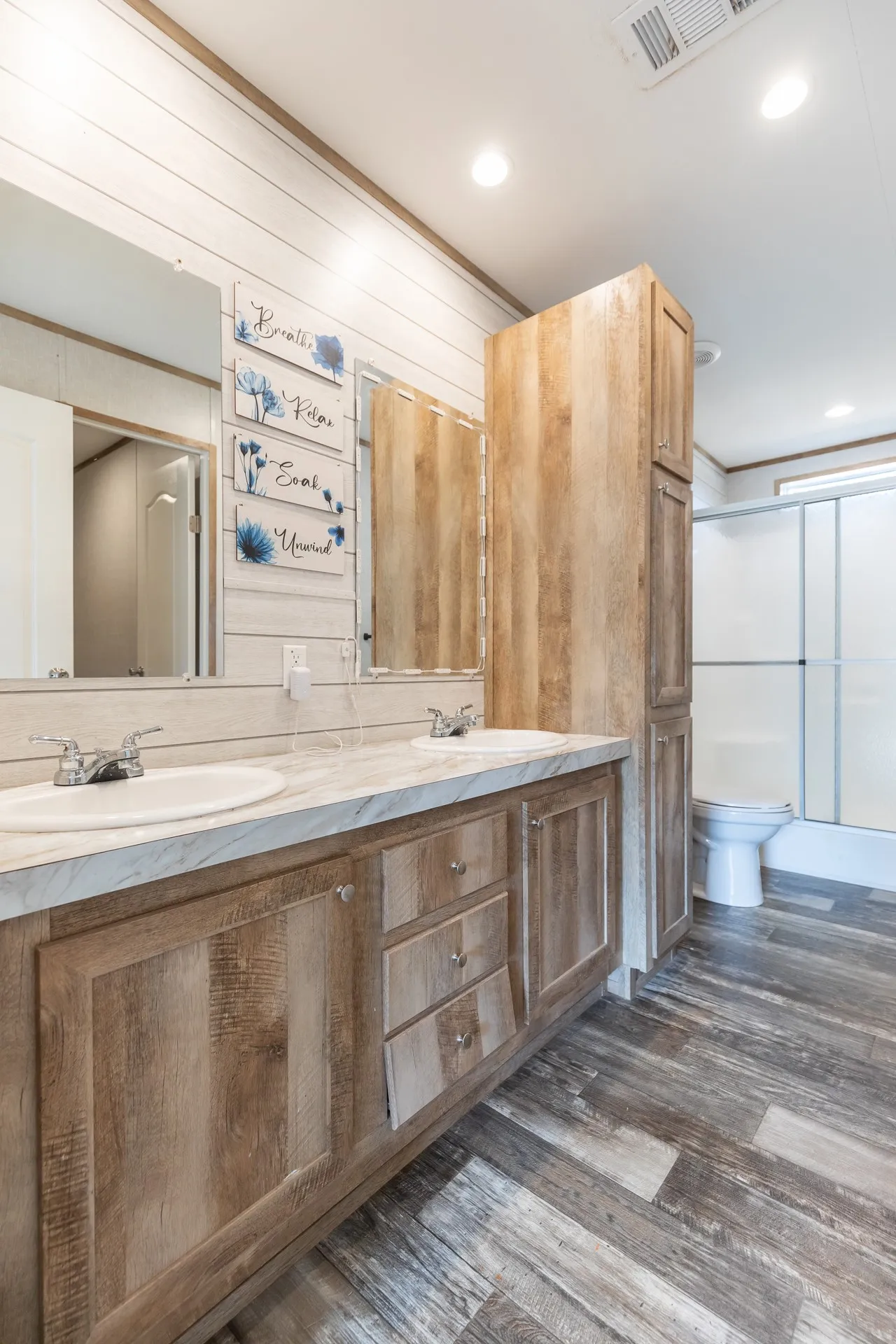 Dual vanity with integrated sinks, ample counter space, custom wood-finish cabinetry, built-in storage tower, and a walk-in shower with sliding glass doors