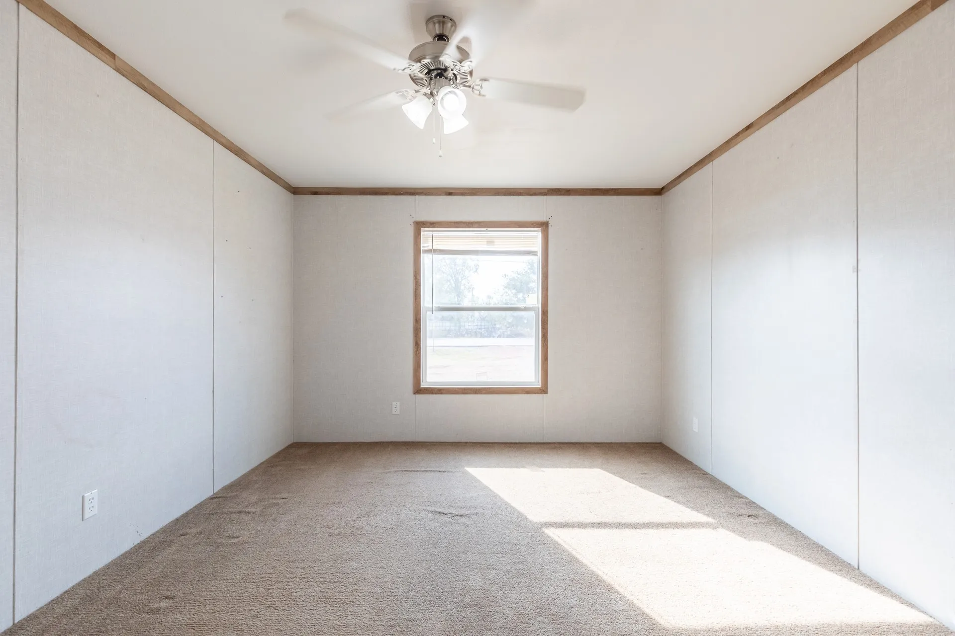 Neutral tone wall paneling with wood-finish trim, a central window with wood-finish casing, and a ceiling fan with integrated lighting