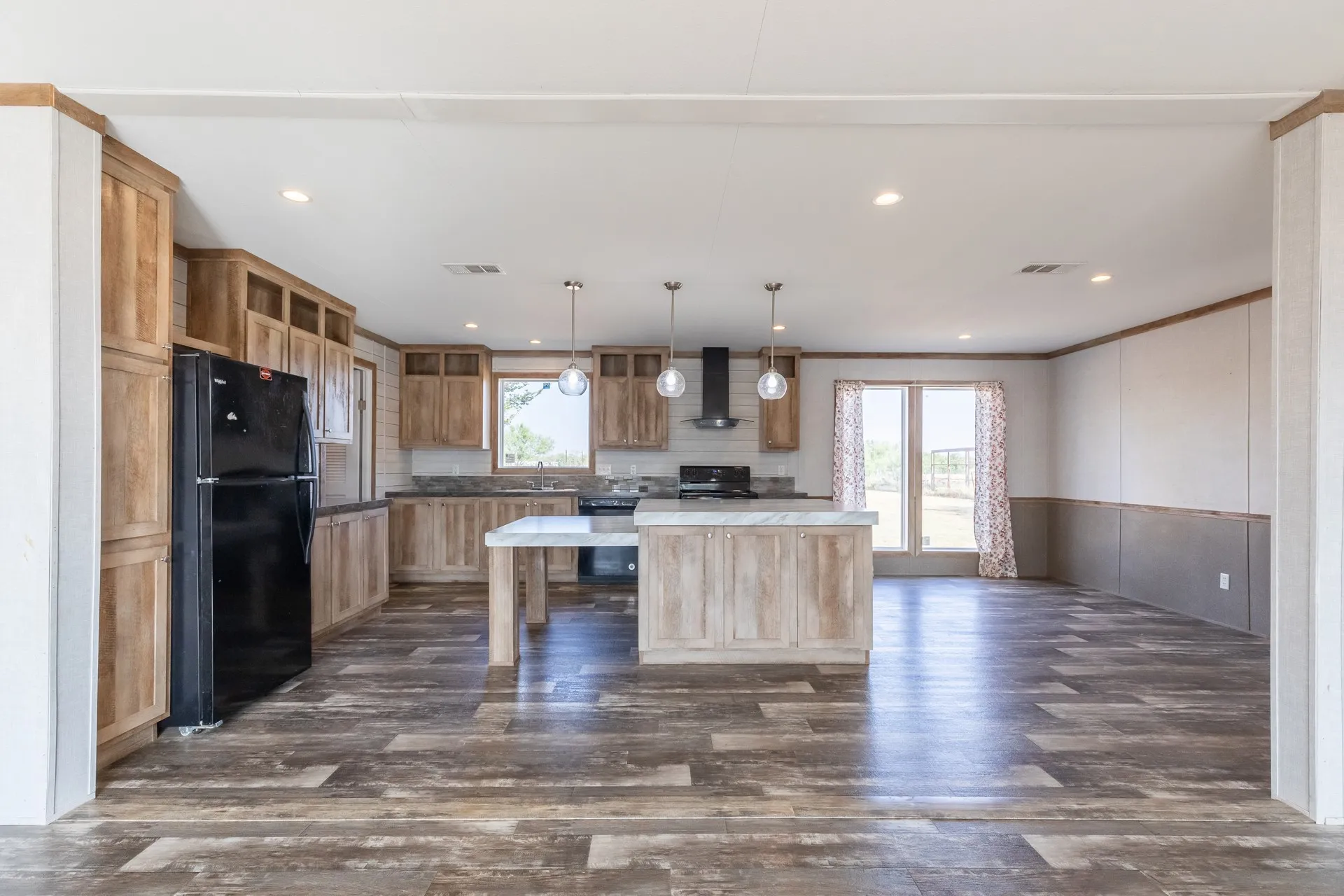 Open-concept kitchen featuring wood-finish cabinetry, a two-tiered island with a stone-finish countertop, stainless steel sink, and wood-finish flooring