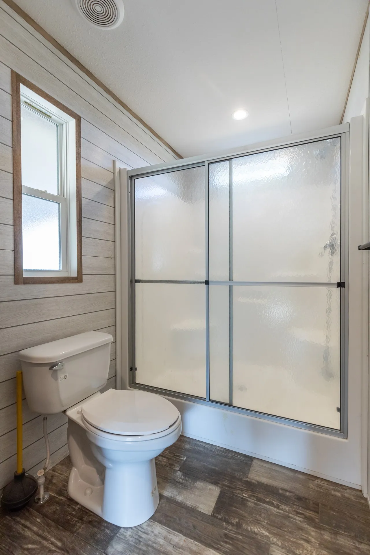 Walk-in shower with sliding glass doors, horizontal paneling on walls, wood-finish flooring, and a single window