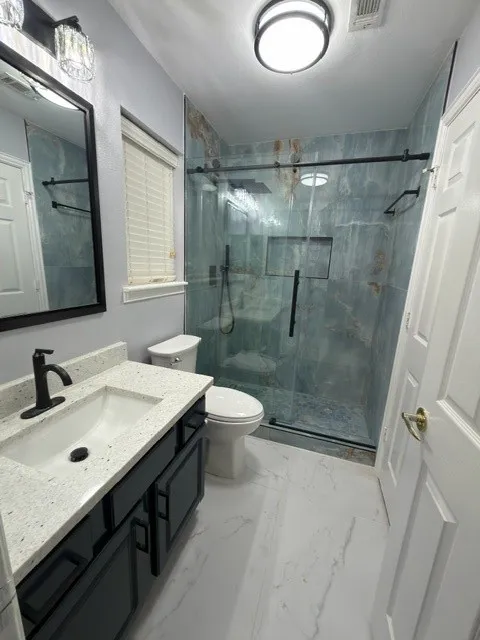 White tile flooring, single vanity with light-colored countertop, dark wood-finish cabinetry, frameless glass shower enclosure, and a tiled shower interior with built-in niches