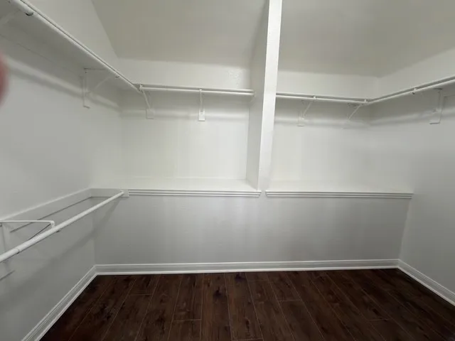 Wood-finish flooring with white baseboards, white walls, and built-in closet shelving