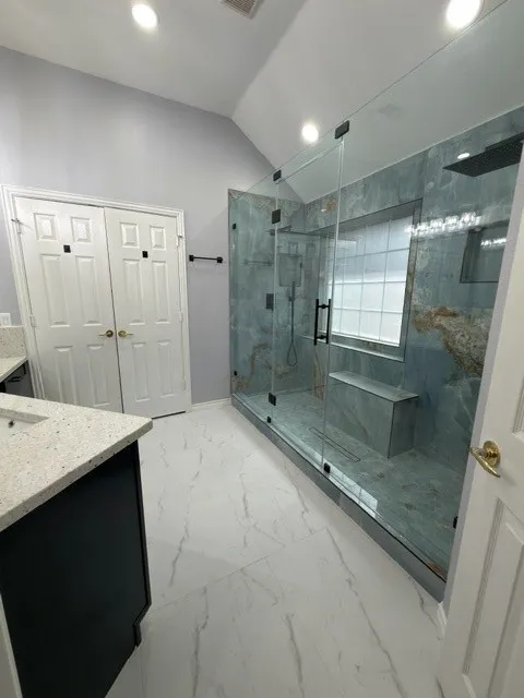 Spacious bathroom featuring a glass-enclosed shower with integrated bench seating, large format wall tiling, and a black-finish rain shower head