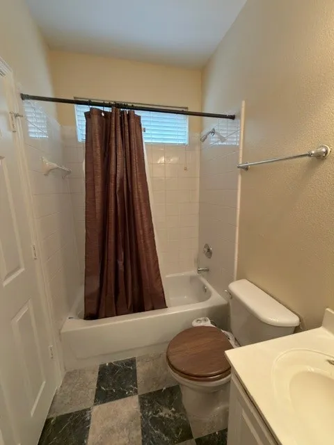 Bathroom featuring a standard tub with white tile surround, a toilet with a wood-finish seat, and checkerboard floor tiles