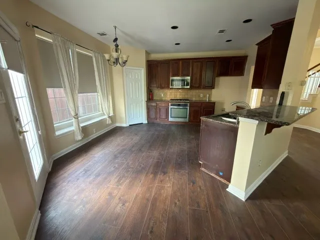 Wood-finish flooring throughout, kitchen with dark wood cabinetry and stainless steel appliances, granite-finish island with integrated sink, chandelier lighting, and multiple windows