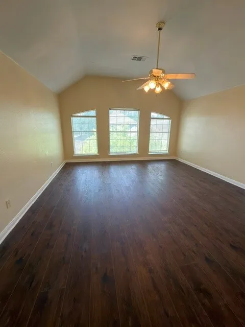 Vaulted ceiling with a ceiling fan, three arched windows, and wood-finish flooring