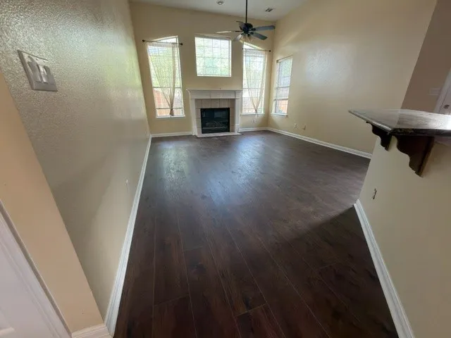 Vaulted ceilings, wood-finish flooring, fireplace with white mantel, multiple windows, and a ceiling fan