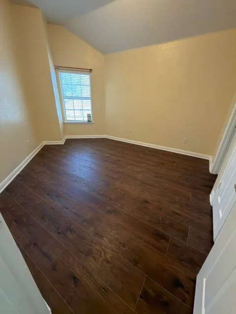 Vaulted ceiling, wood-finish flooring, natural light through a single window, window blinds, and white trim molding