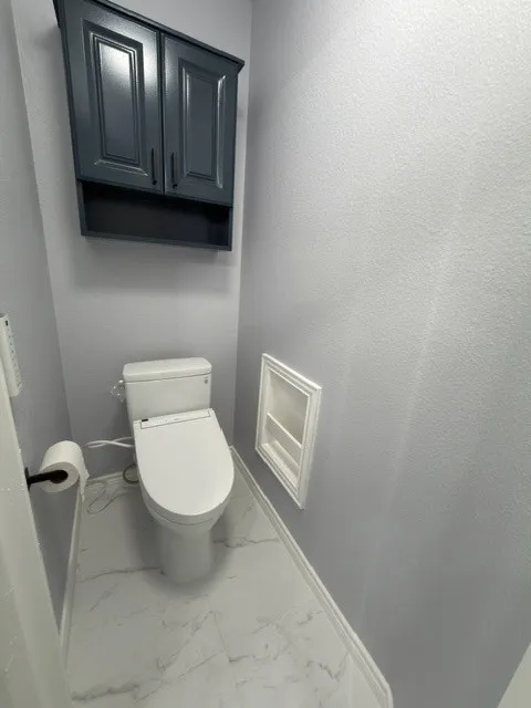 White marble-look flooring, built-in wall cabinet, and a modern toilet