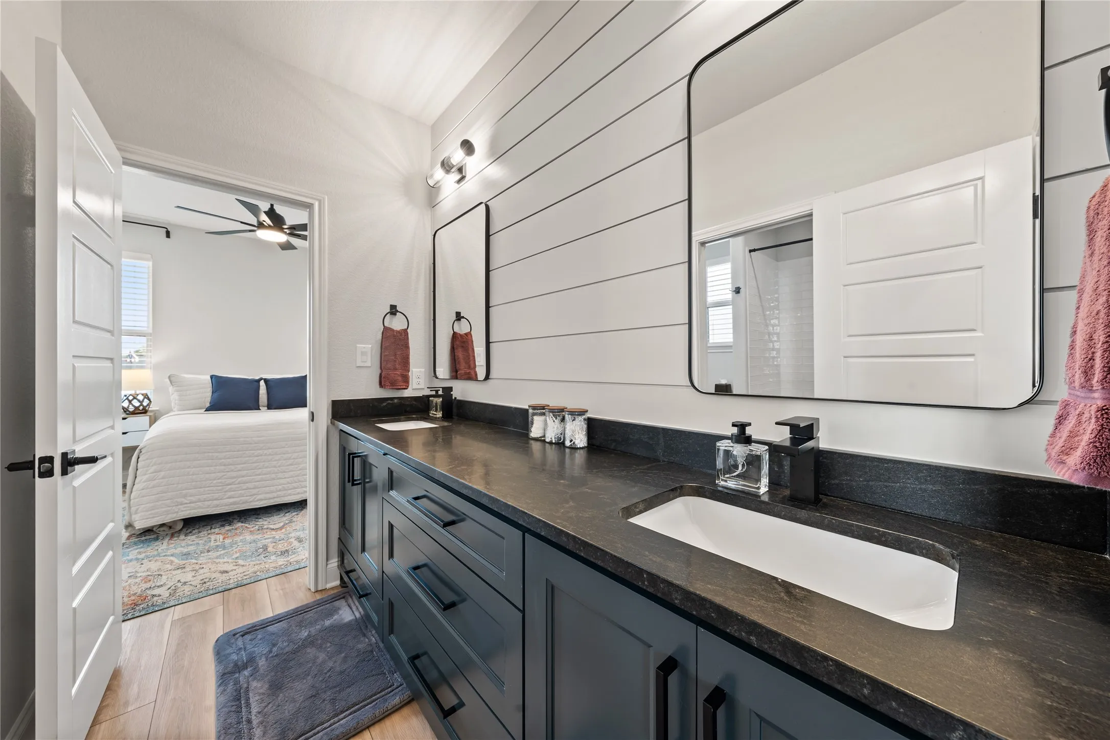 Dual vanity with an integrated sink, dark countertop, black fixtures, and shiplap accent wall