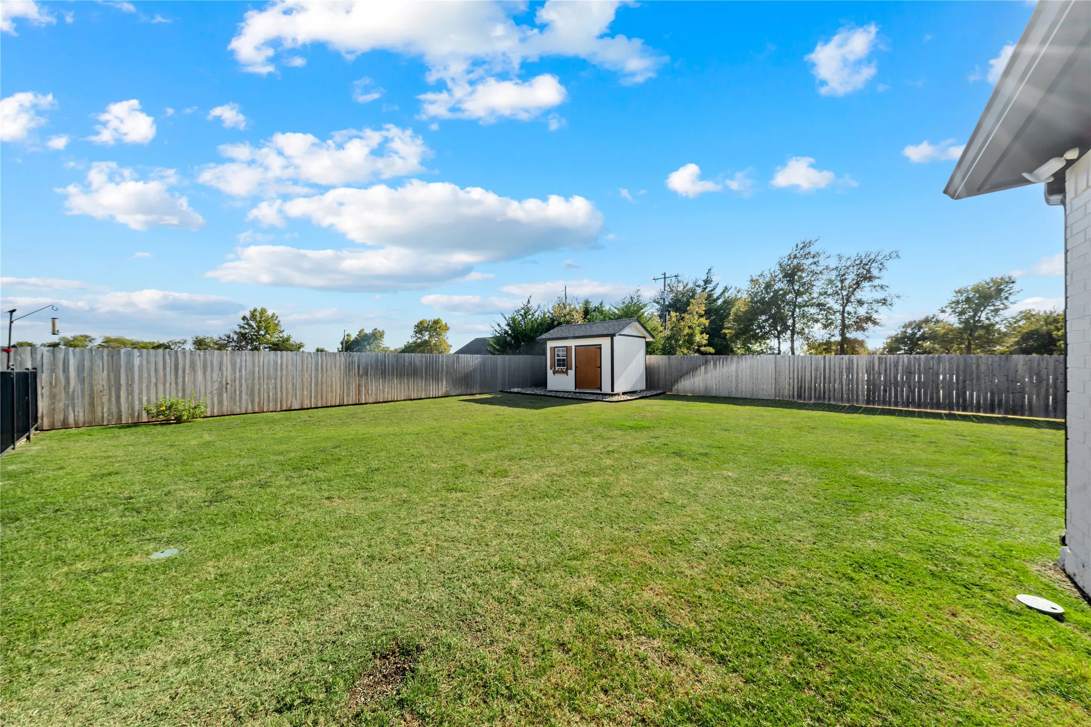 Expansive fenced backyard featuring a manicured lawn and a utility shed with a gable roof