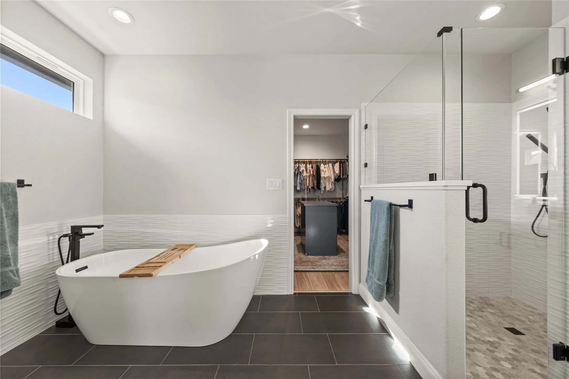 Freestanding soaking tub, walk-in shower with glass enclosure, dark tile flooring, textured wall tile, and recessed lighting