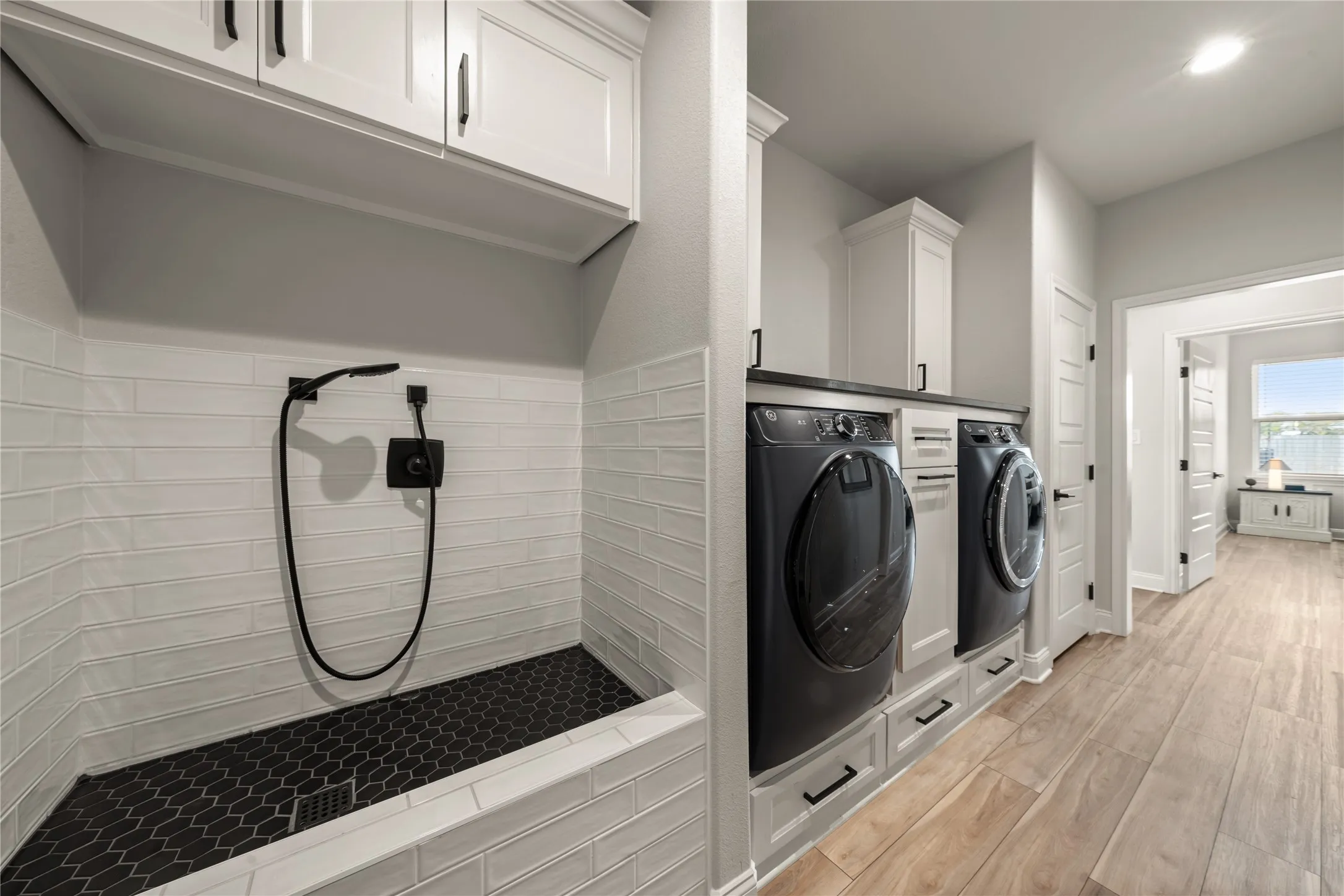 Laundry area featuring integrated appliances, white cabinetry, dark countertops, and wood-finish flooring