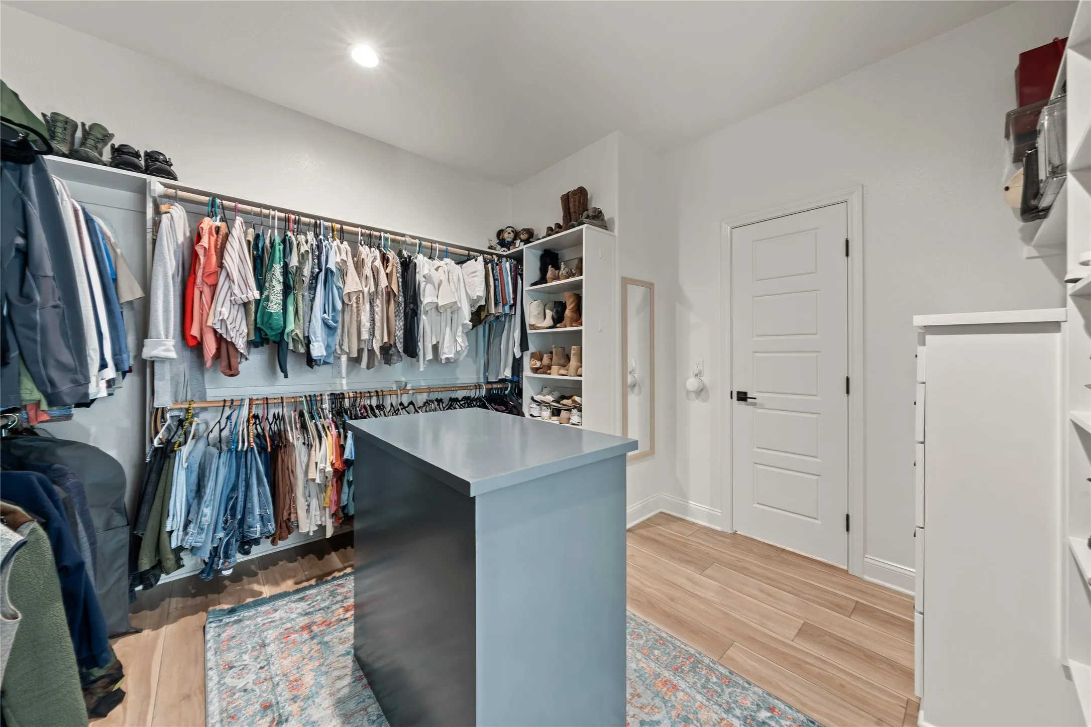 Custom closet system featuring a central island, wood-finish flooring, recessed lighting, and white paneled doors