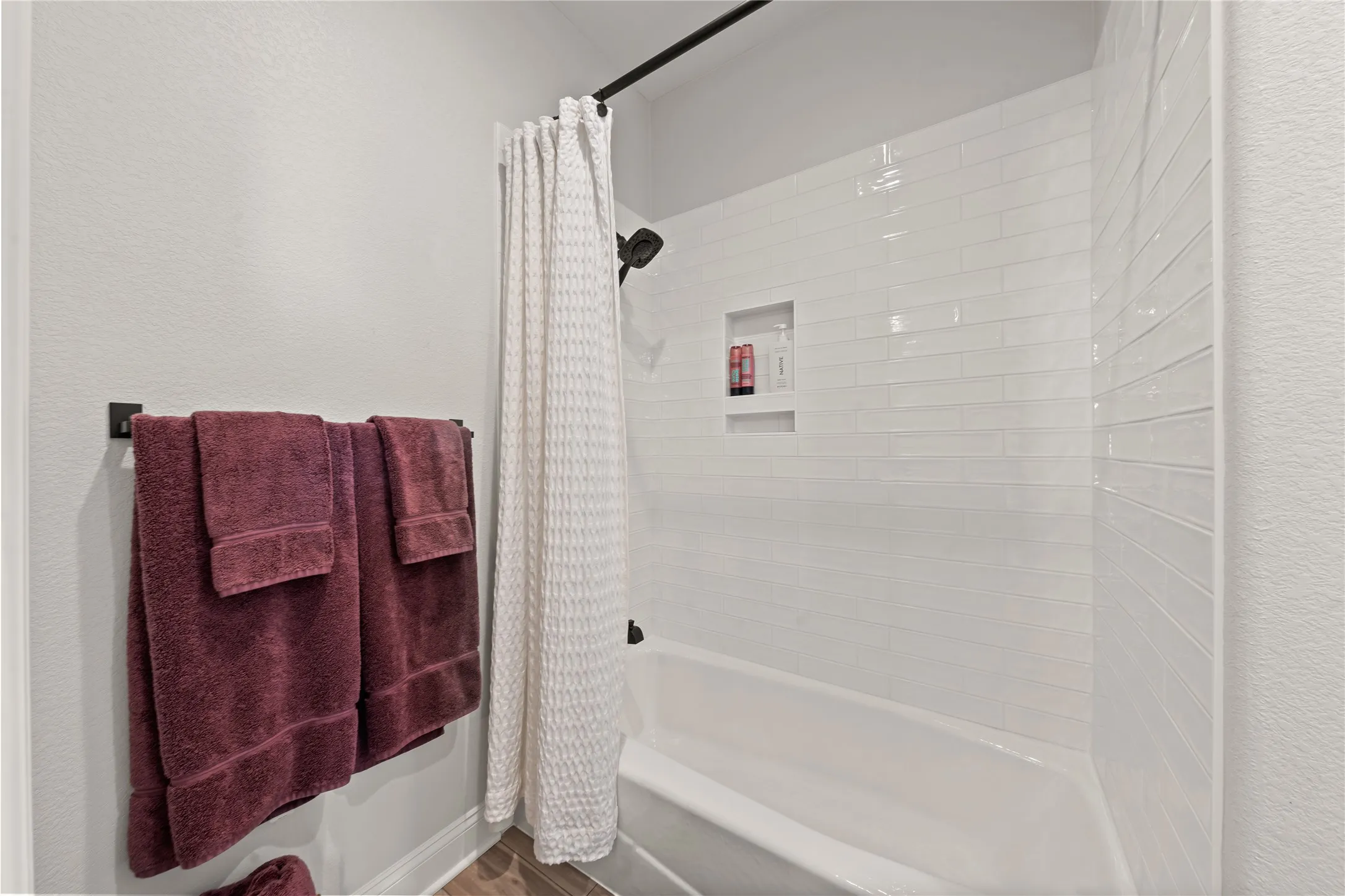 Bathtub with subway tile surround, integrated shower niche, and matte black shower fixtures