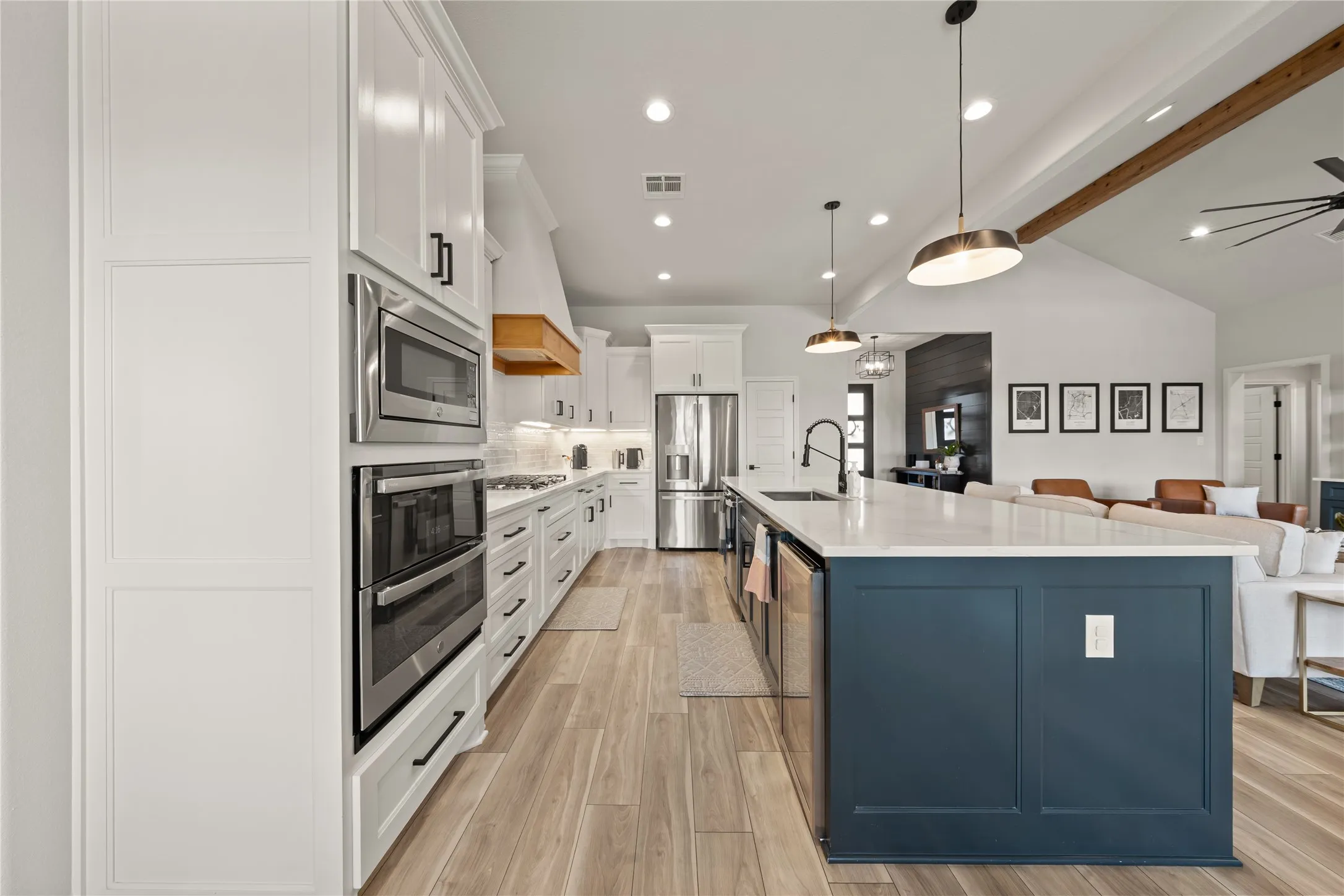 Kitchen featuring white shaker cabinetry, stainless steel appliances, a large center island with a dark base, light countertops, and wood-finish flooring