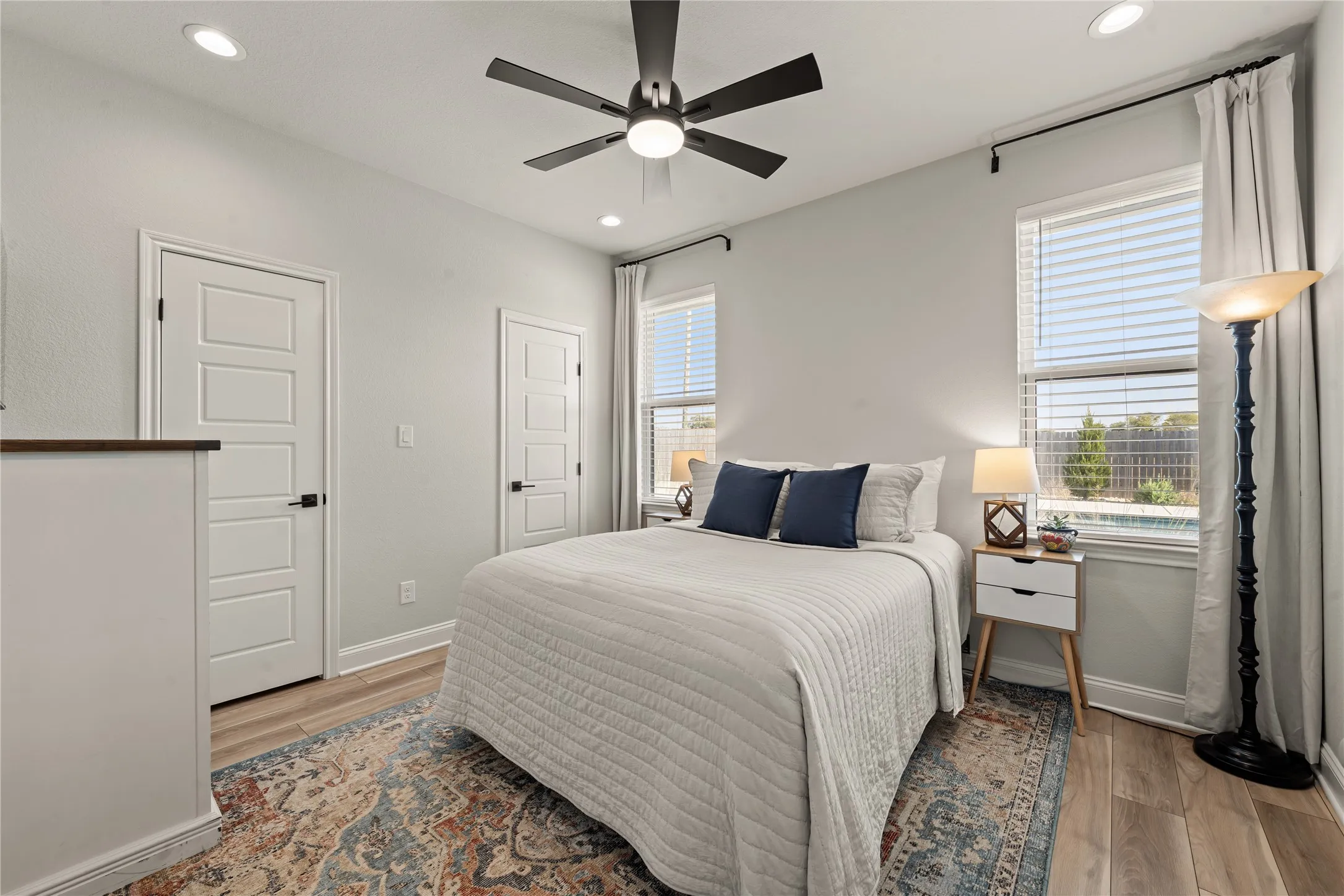 Recessed lighting, ceiling fan, wood-finish flooring, white paneled doors with black hardware, and two windows