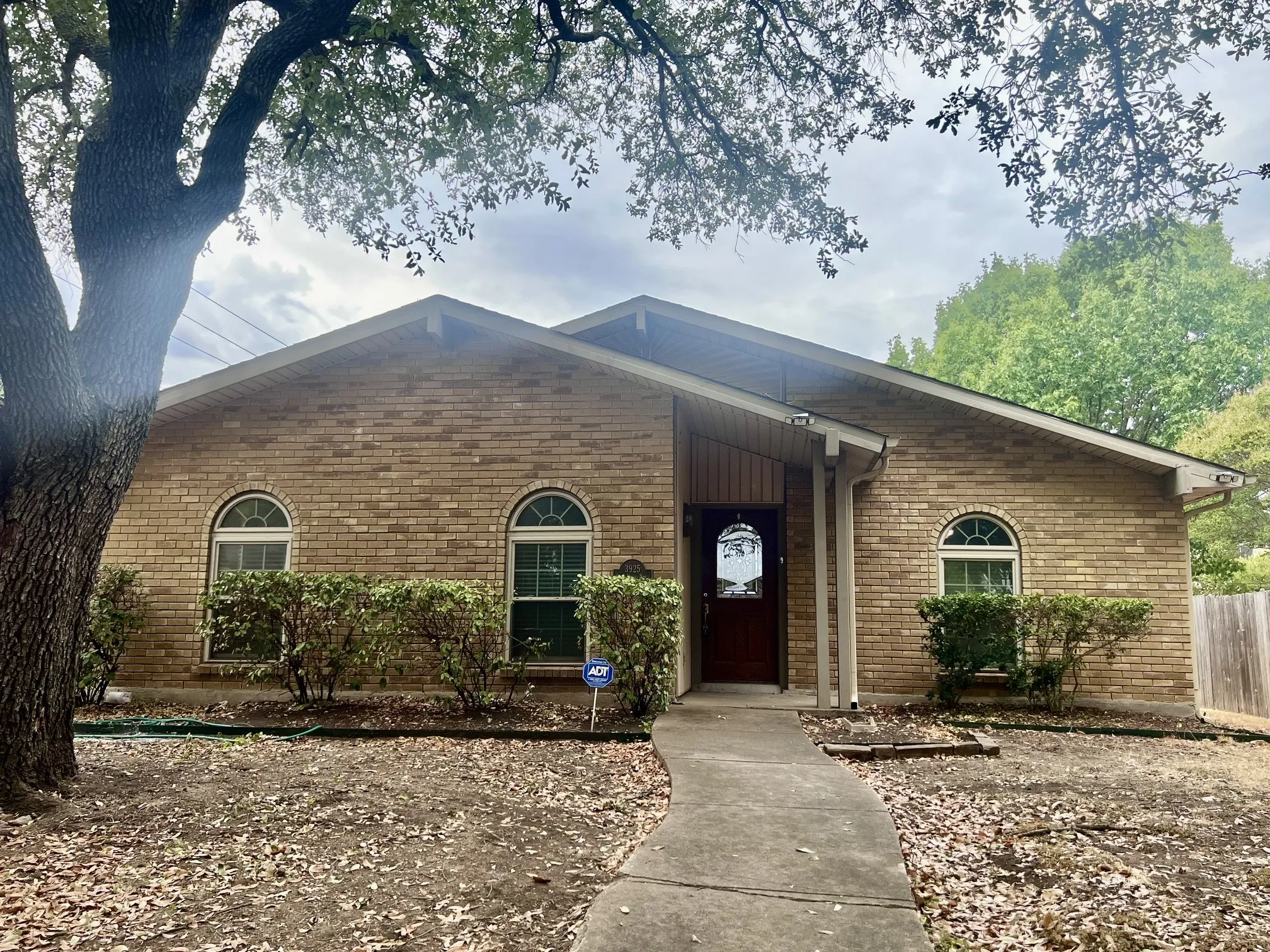 Brick exterior with arched windows, covered entryway, and mature trees