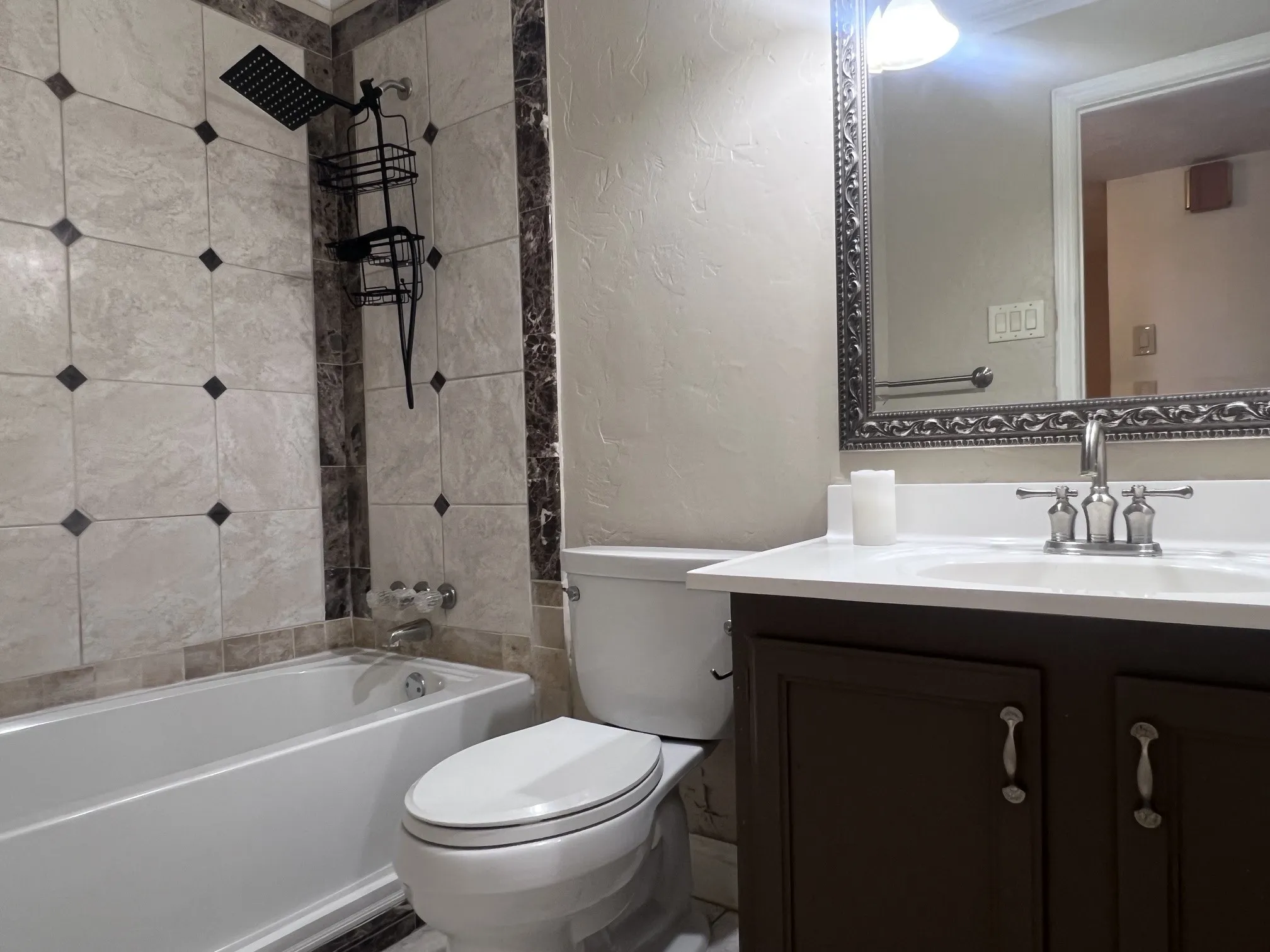Bathtub with tiled surround, rain shower head, toilet, vanity with integrated sink, and framed mirror