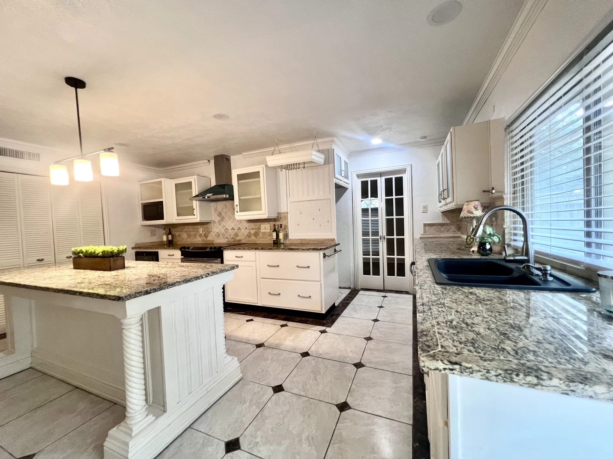 Kitchen featuring a center island with granite countertops, white cabinetry, a tile backsplash, and a black sink with a gooseneck faucet