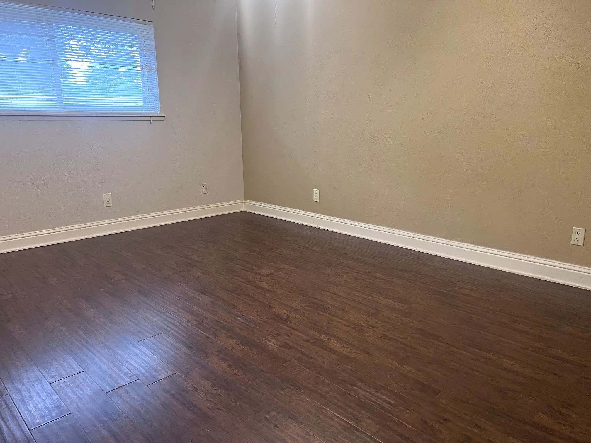 Wood-finish flooring with white trim and a window with blinds