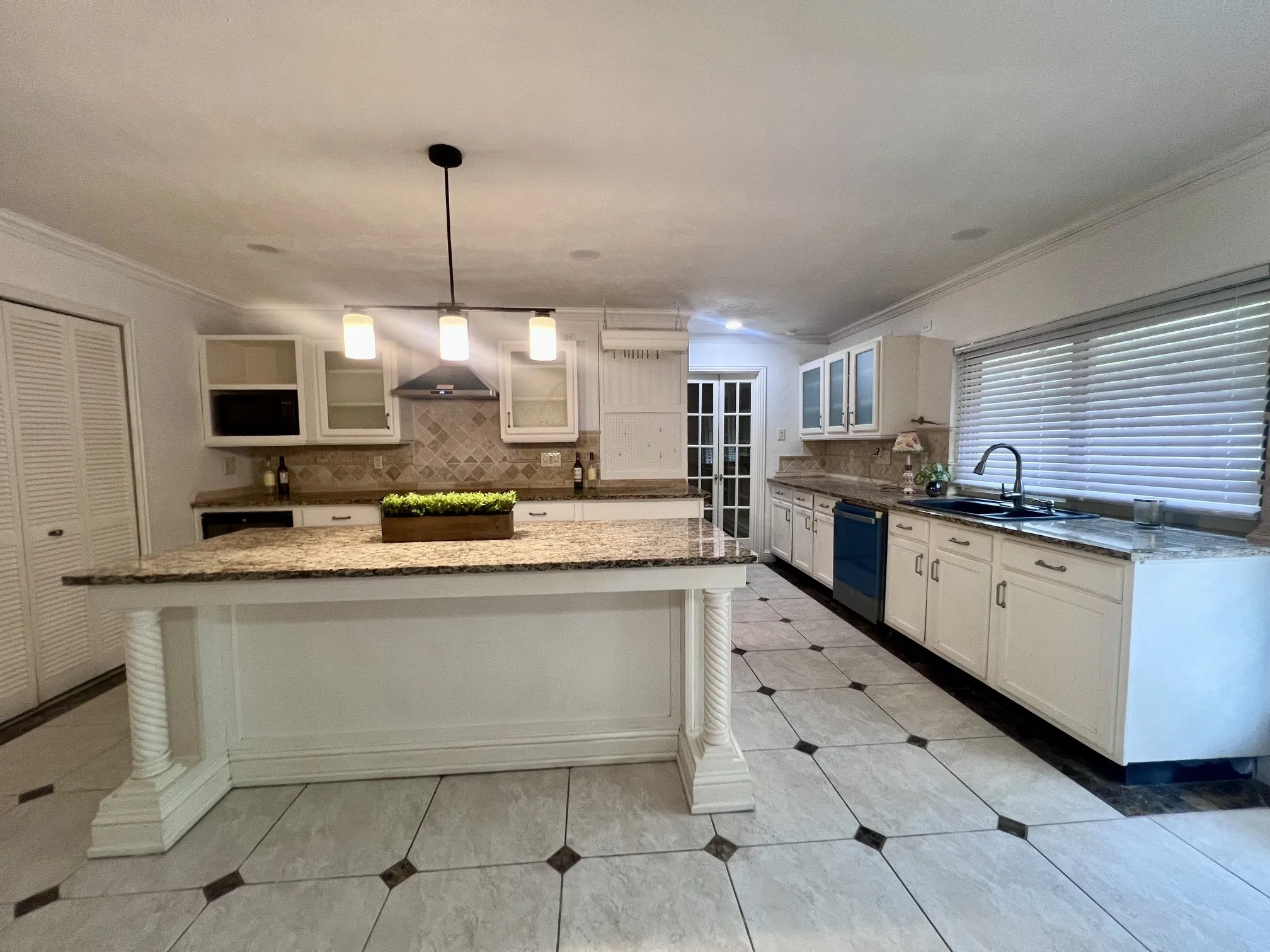 Kitchen island with granite countertop, tiled flooring, white cabinetry, dark appliances, and a modern pendant light fixture