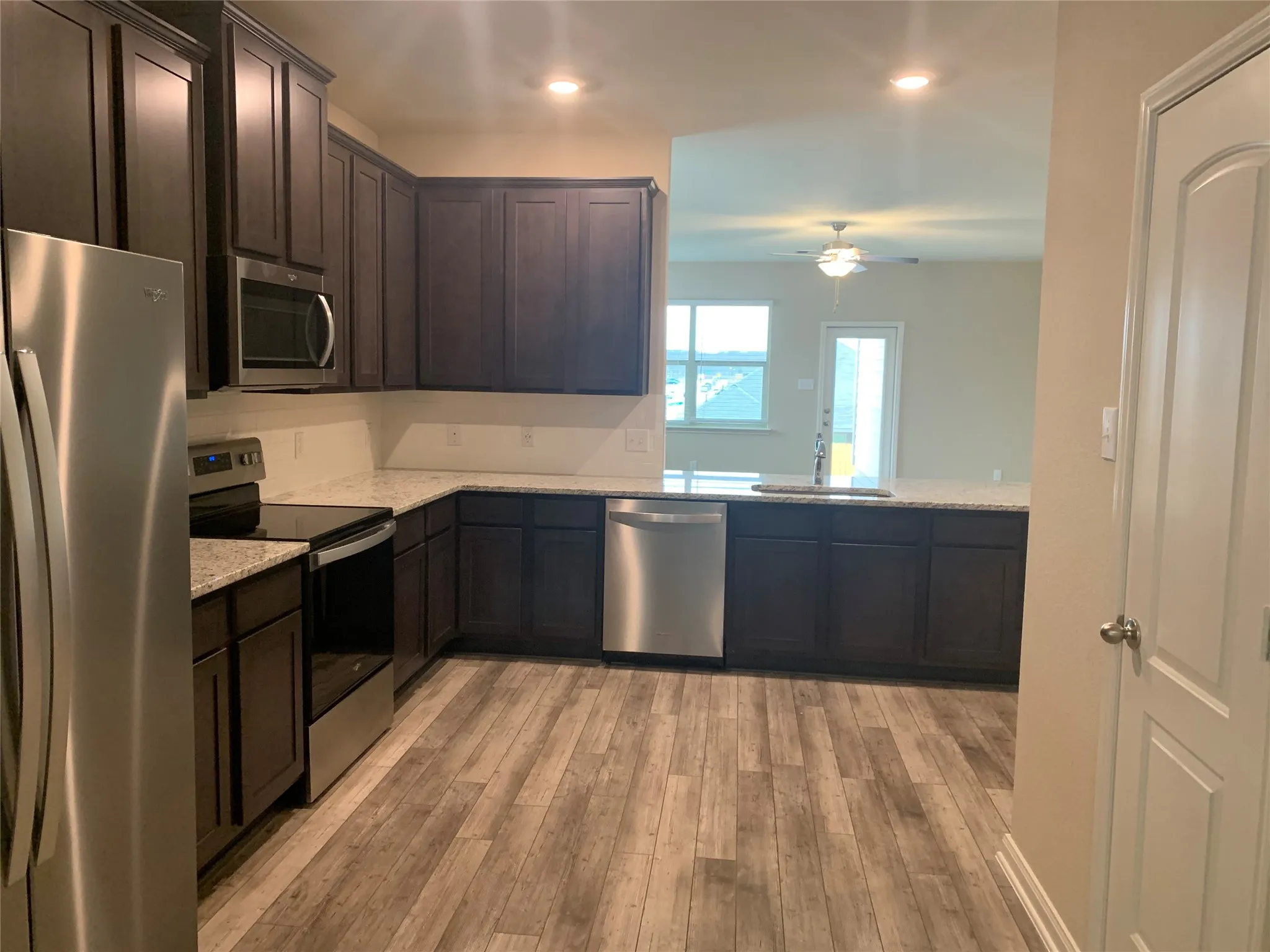 Kitchen featuring wood-finish flooring, dark wood cabinetry, light speckled countertops, and stainless steel appliances