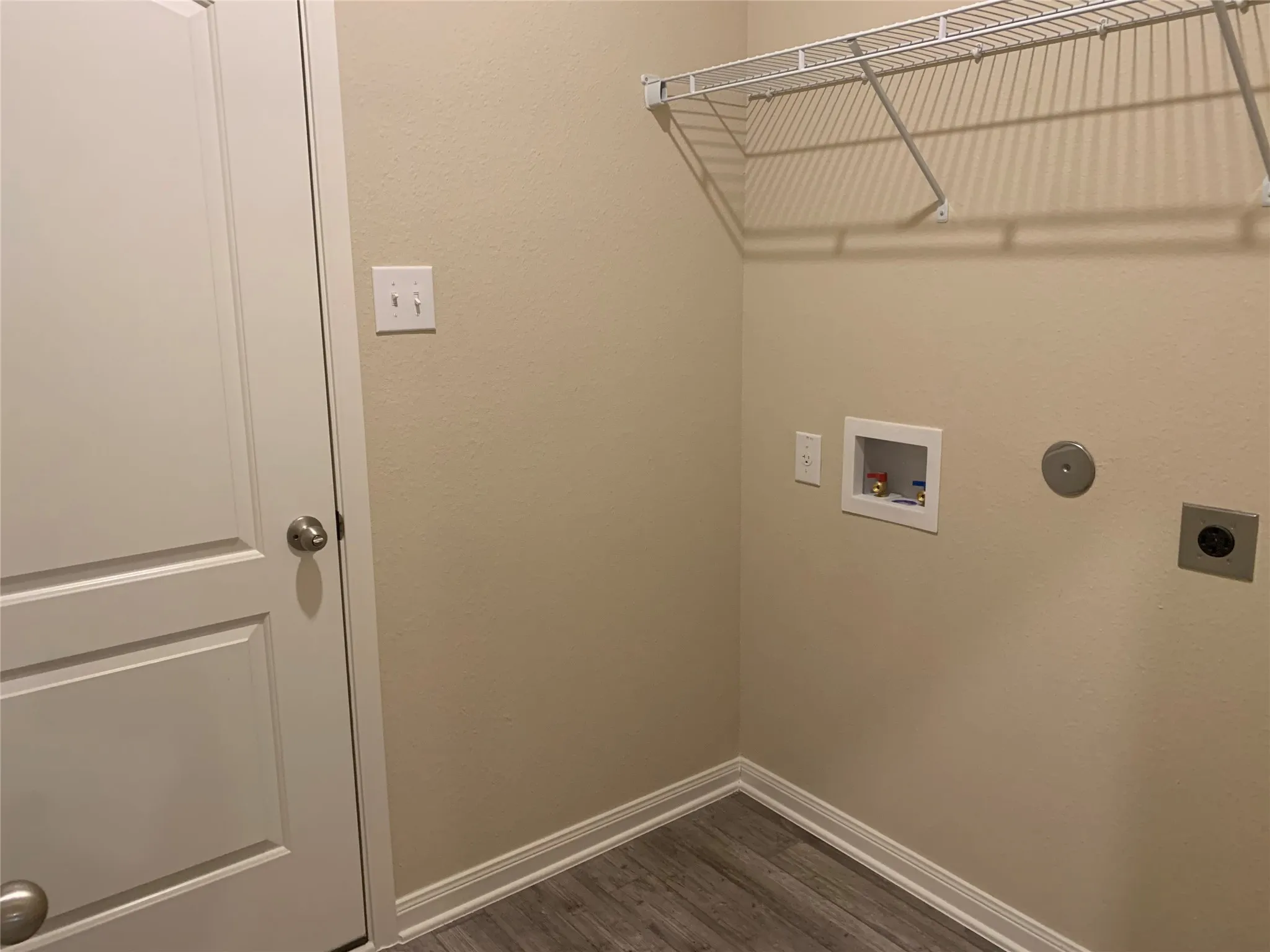 Laundry area featuring wire shelving, utility hookups, and wood-finish flooring