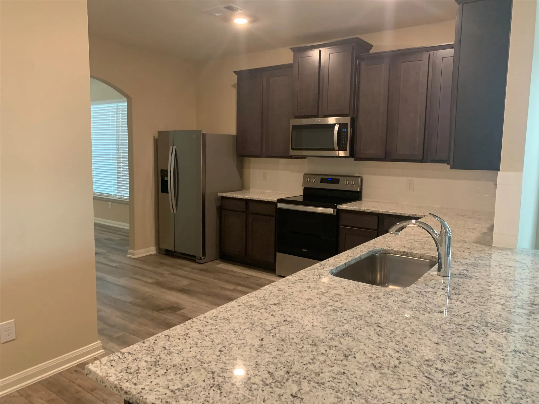 Granite countertops, stainless steel appliances, dark wood cabinetry, and wood-finish flooring