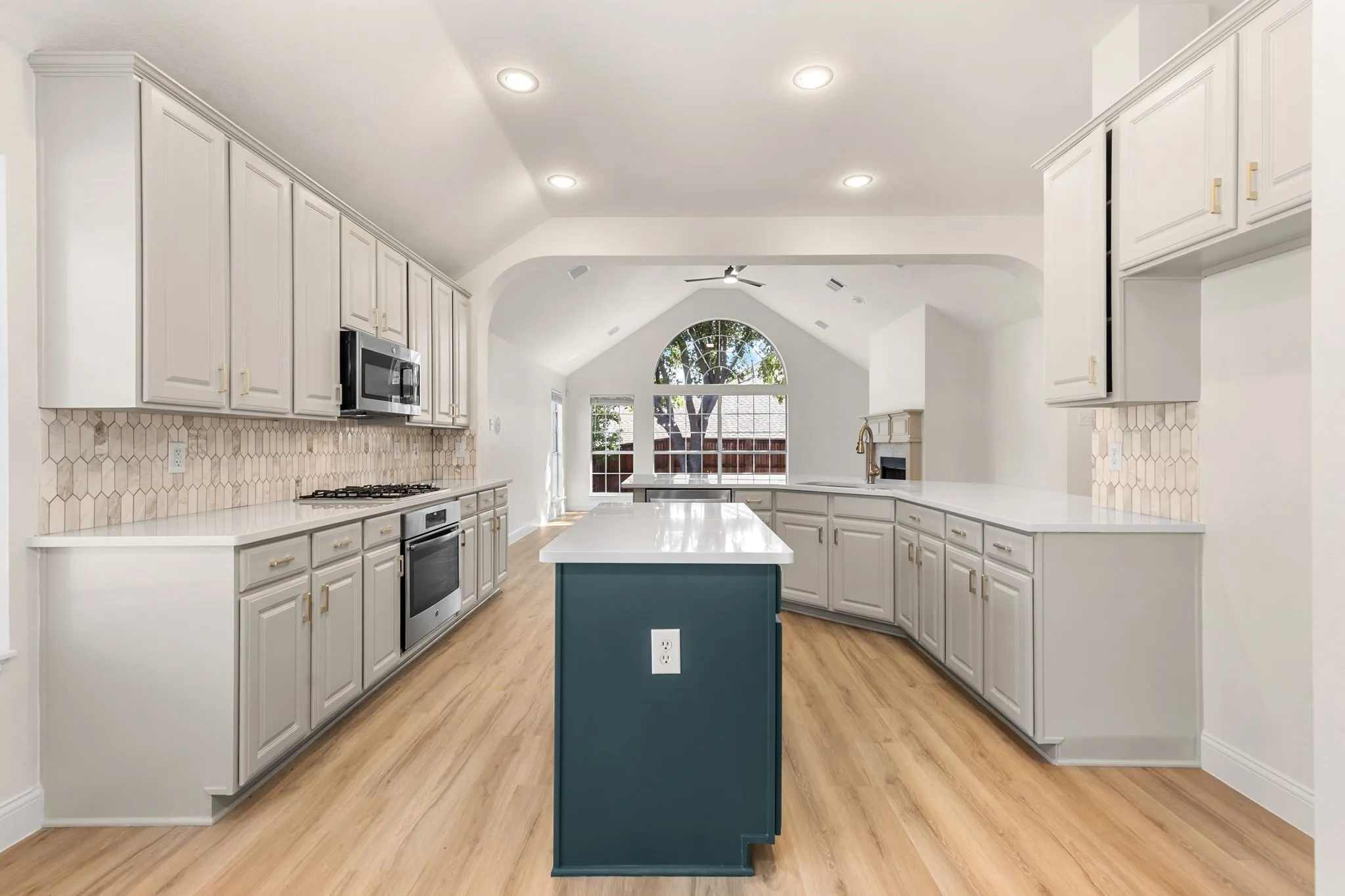 Open-concept kitchen featuring an accent island, recessed lighting, wood-finish flooring, and light-toned cabinetry with a patterned backsplash