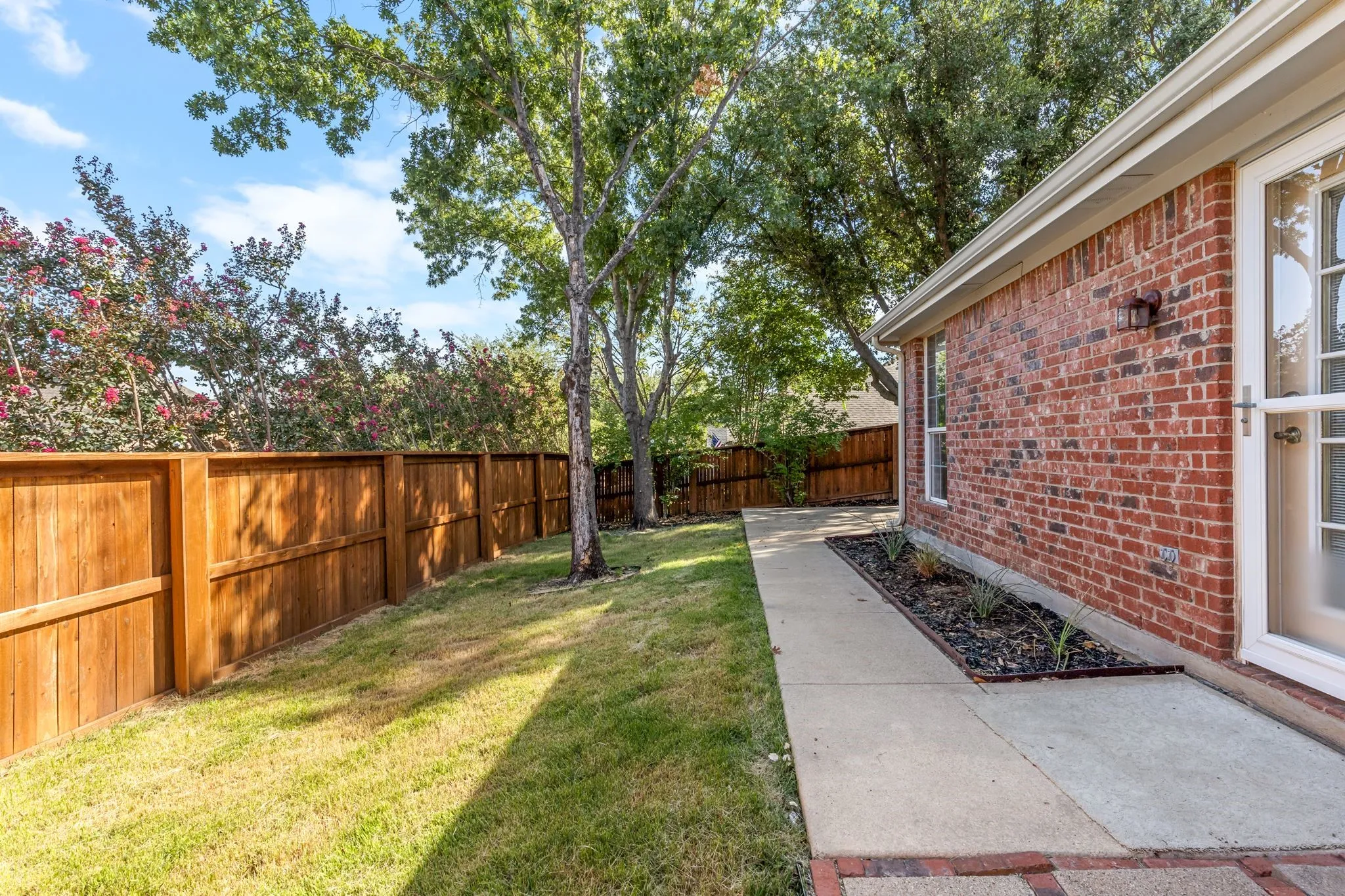 Red brick exterior with white framed windows, complete with a concrete walkway and a planter bed