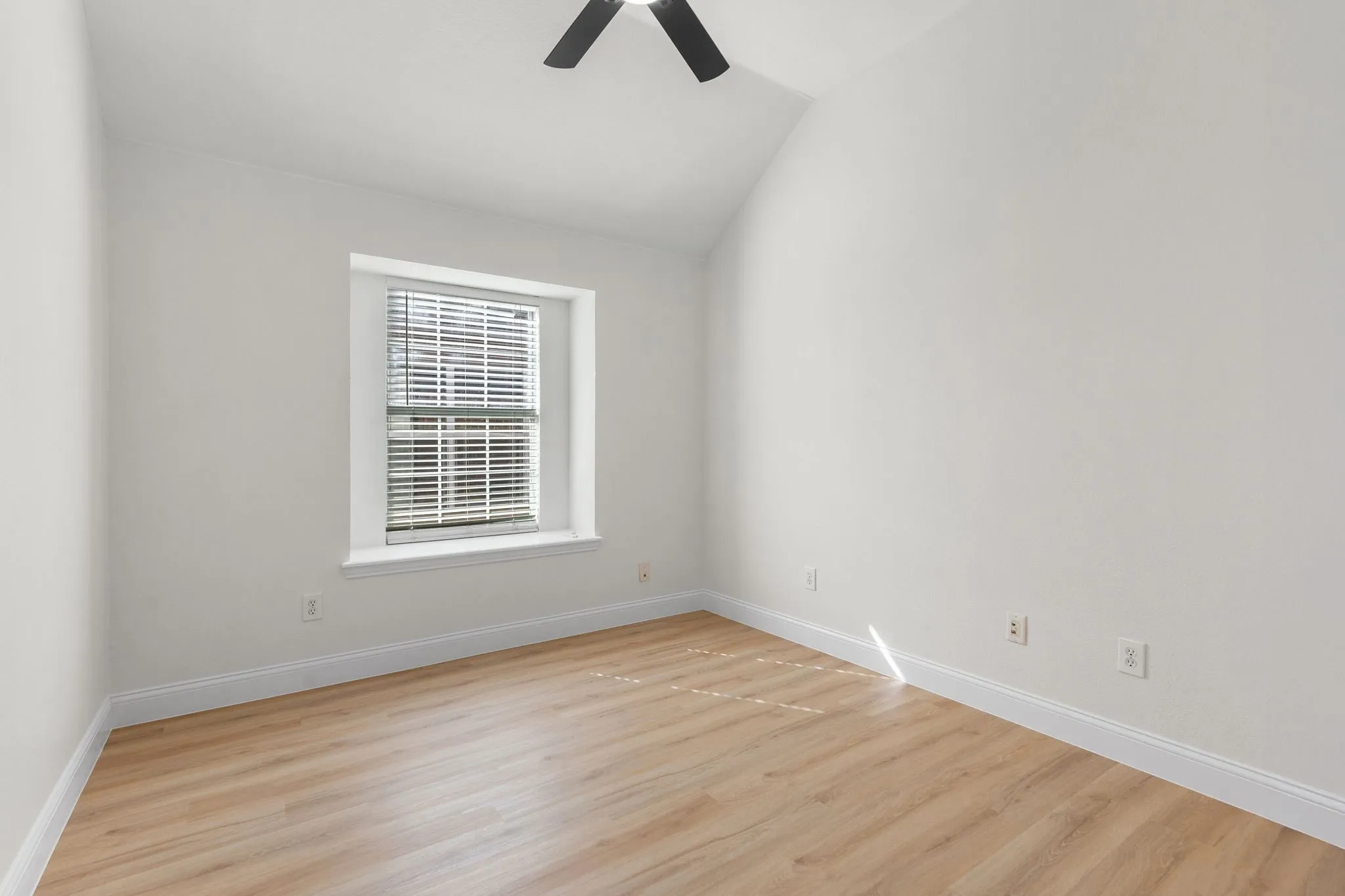 Bright interior with a vaulted ceiling, wood-finish flooring, a window with blinds, and a ceiling fan