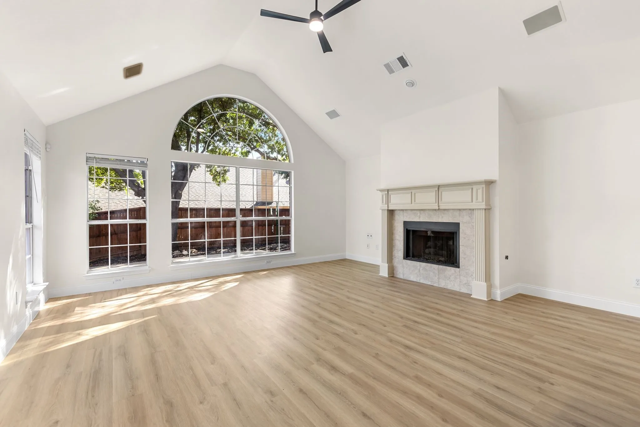 Vaulted ceiling with an architectural arched window, wood-finish flooring, and a fireplace with a decorative mantel and hearth