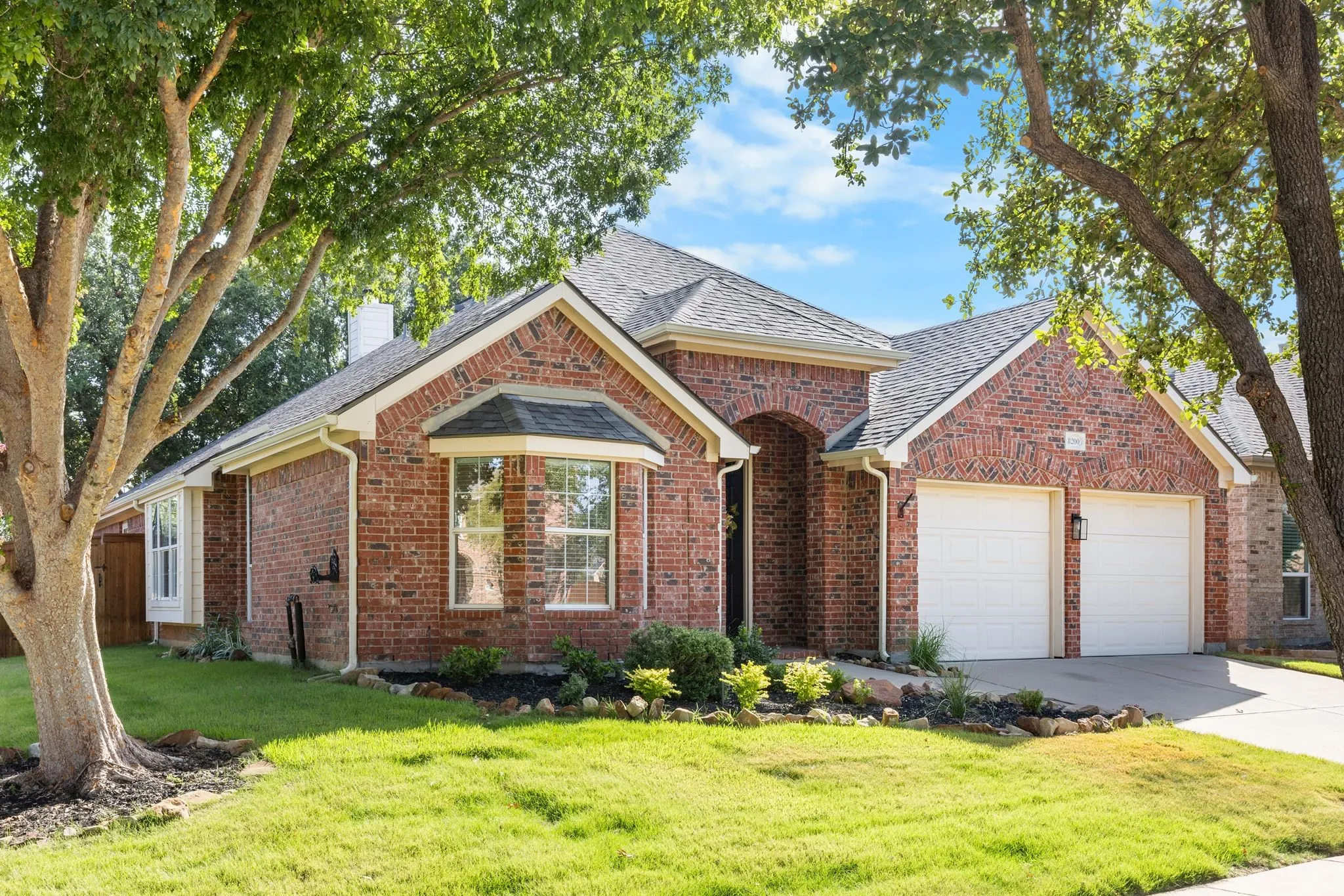 Red brick exterior with white trim, bay window, two-car garage, and established landscaping