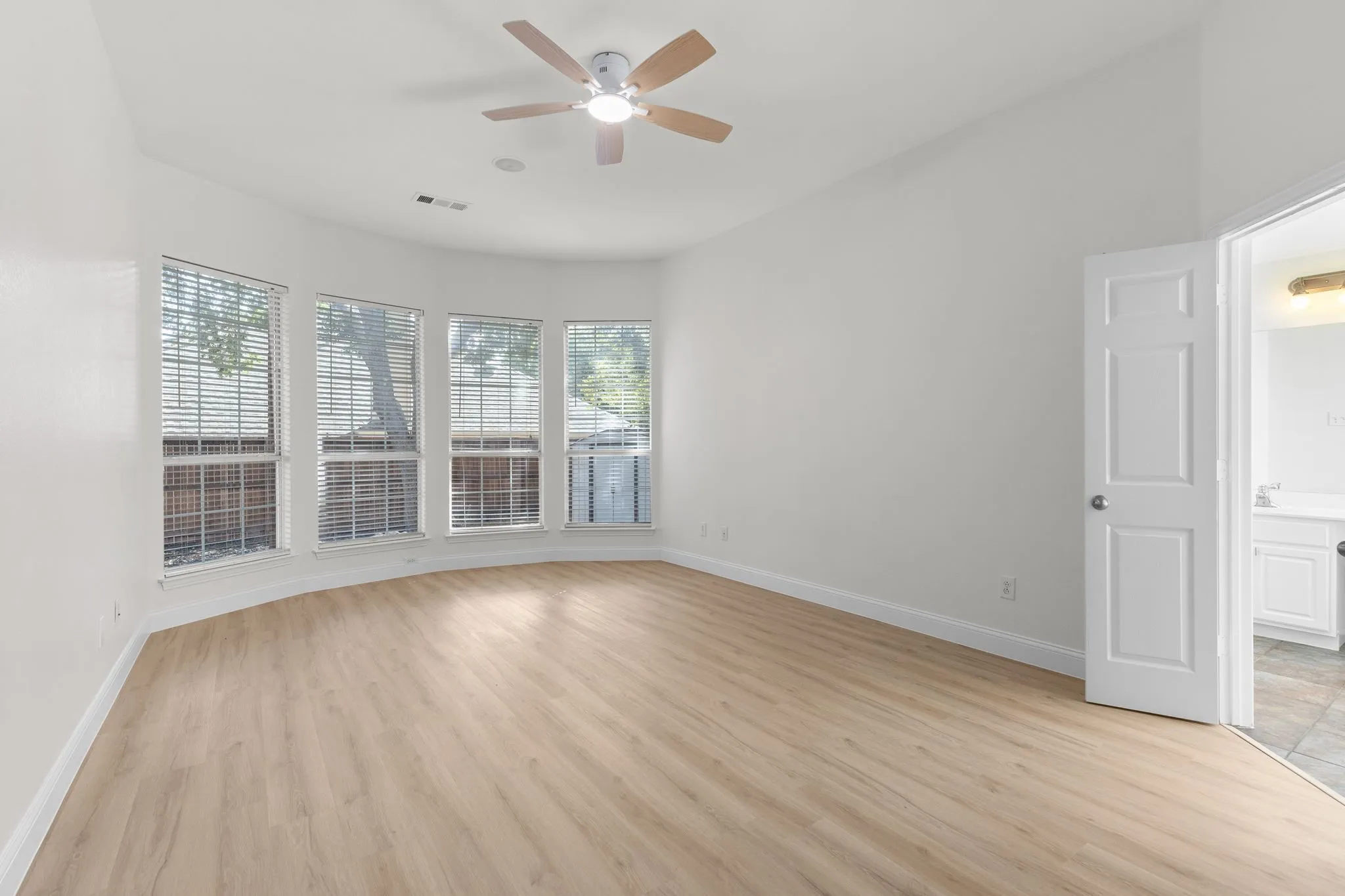 Vaulted ceiling room featuring light wood-finish flooring, a ceiling fan with light, and a bay window with multiple vertical blinds