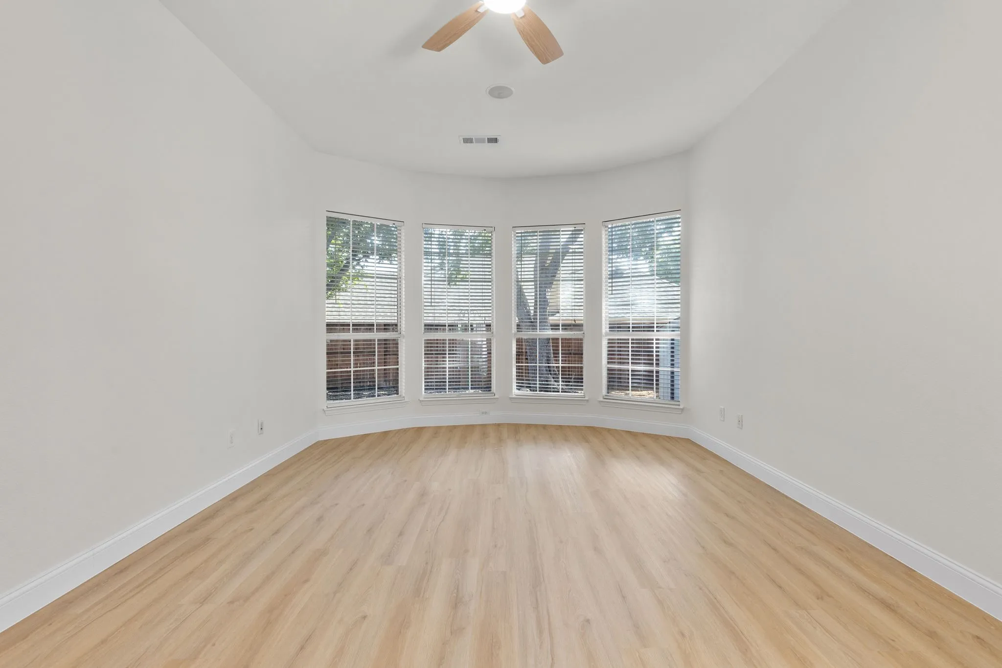 Curved wall with four windows, wood-finish flooring, white walls, and a ceiling fan