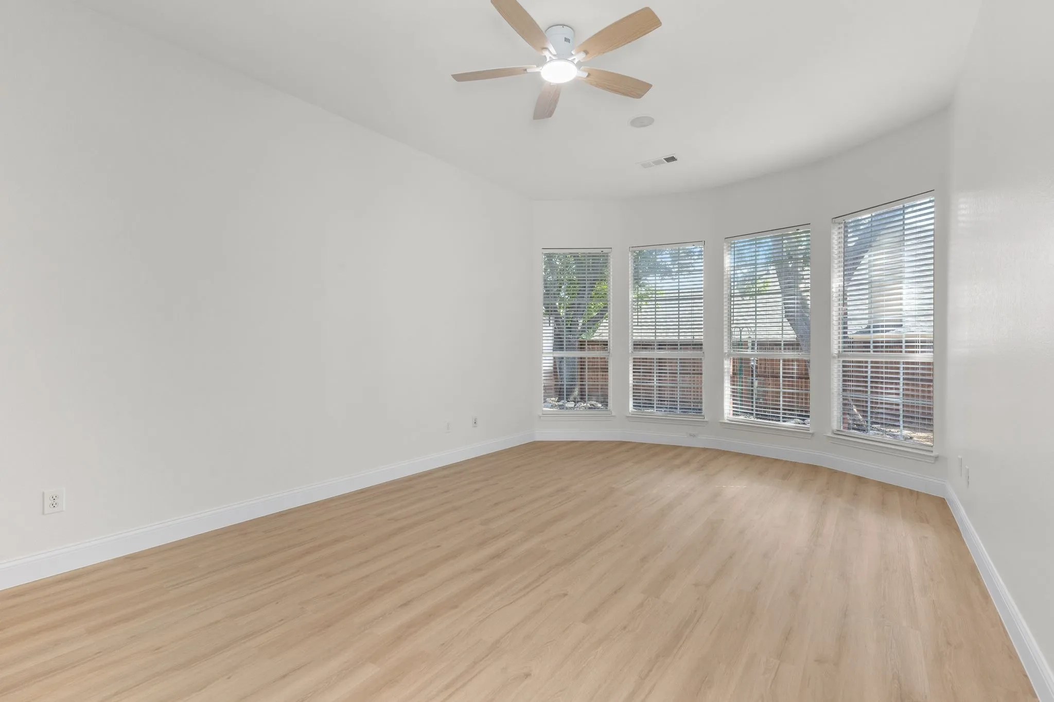 Curved wall featuring multiple windows with blinds, wood-finish flooring, and a ceiling fan with integrated lighting