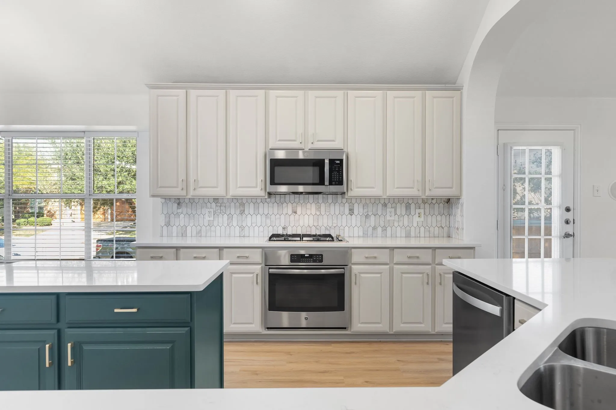 Kitchen featuring light-toned cabinetry, stainless steel appliances, a patterned tile backsplash, and a central island with contrasting dark-toned cabinetry and a white countertop