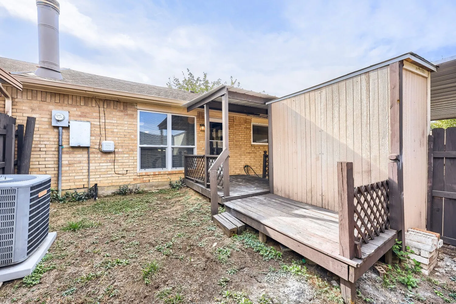 Brick exterior with covered deck, lattice railing, and a detached storage structure