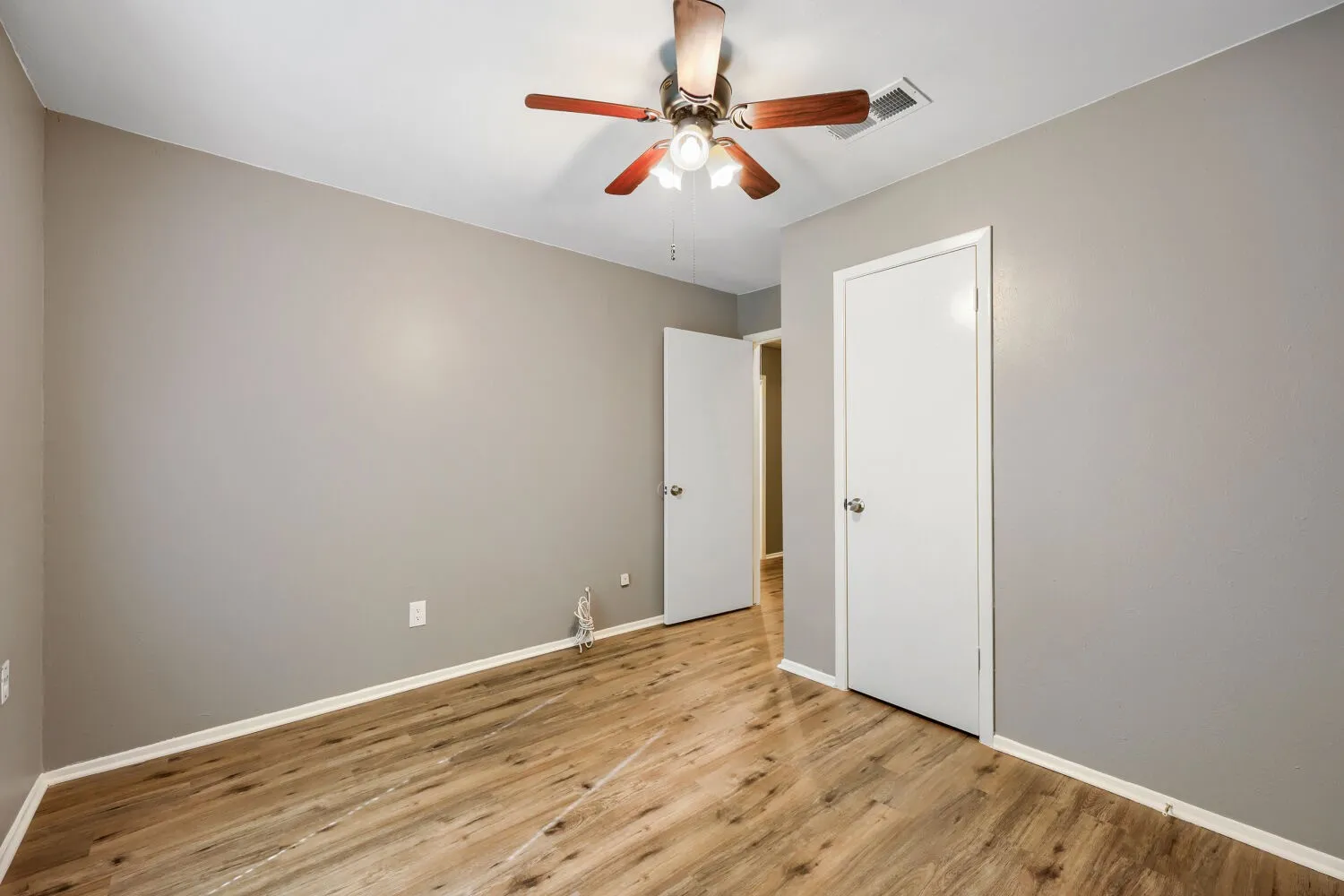Wood-finish flooring, light gray wall tones, ceiling-mounted fan with light fixture, and white painted doors