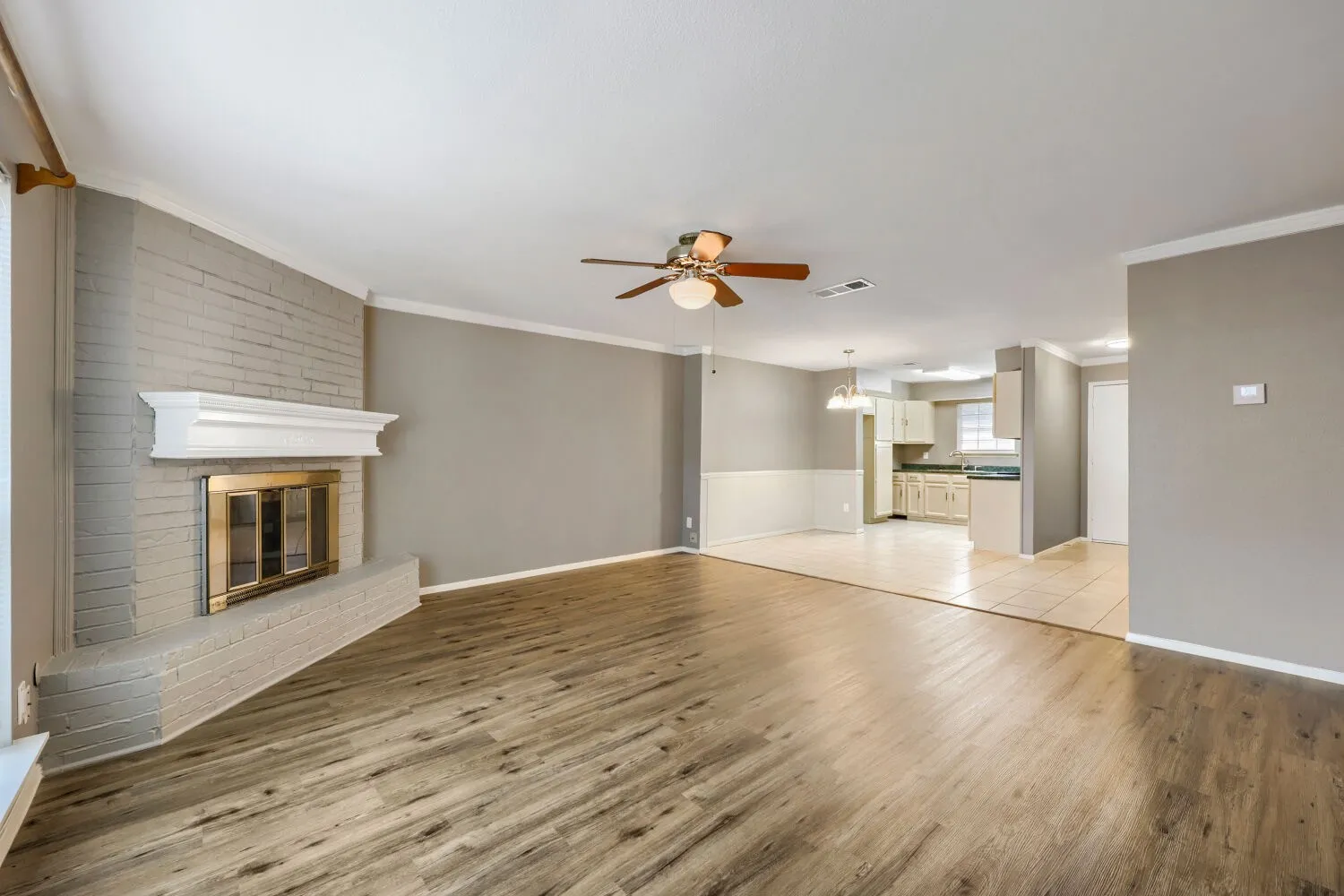 Open-concept living space with wood-finish flooring, a brick fireplace, and a ceiling fan
