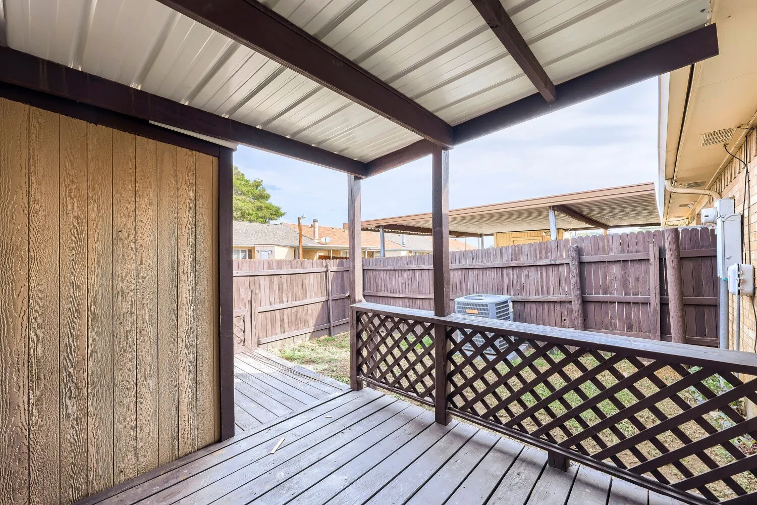 Covered outdoor patio with a corrugated metal roof, wood-finish decking, and a lattice-patterned railing