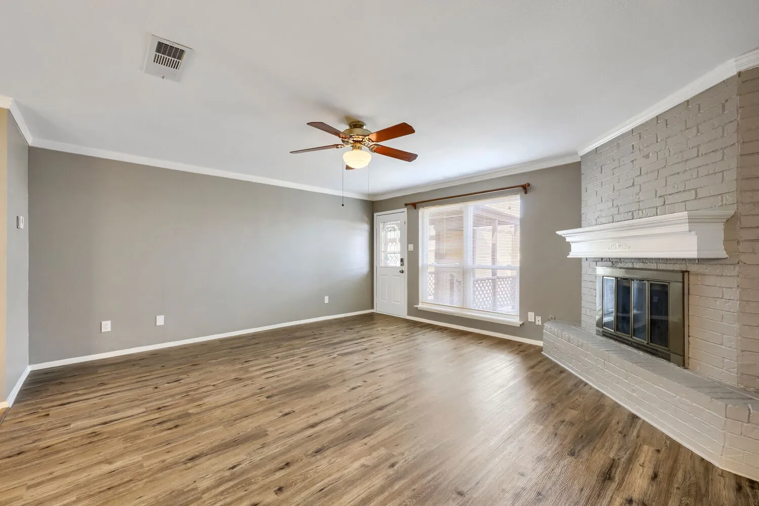 Wood-finish flooring, crown molding, and a painted brick fireplace with a white mantel