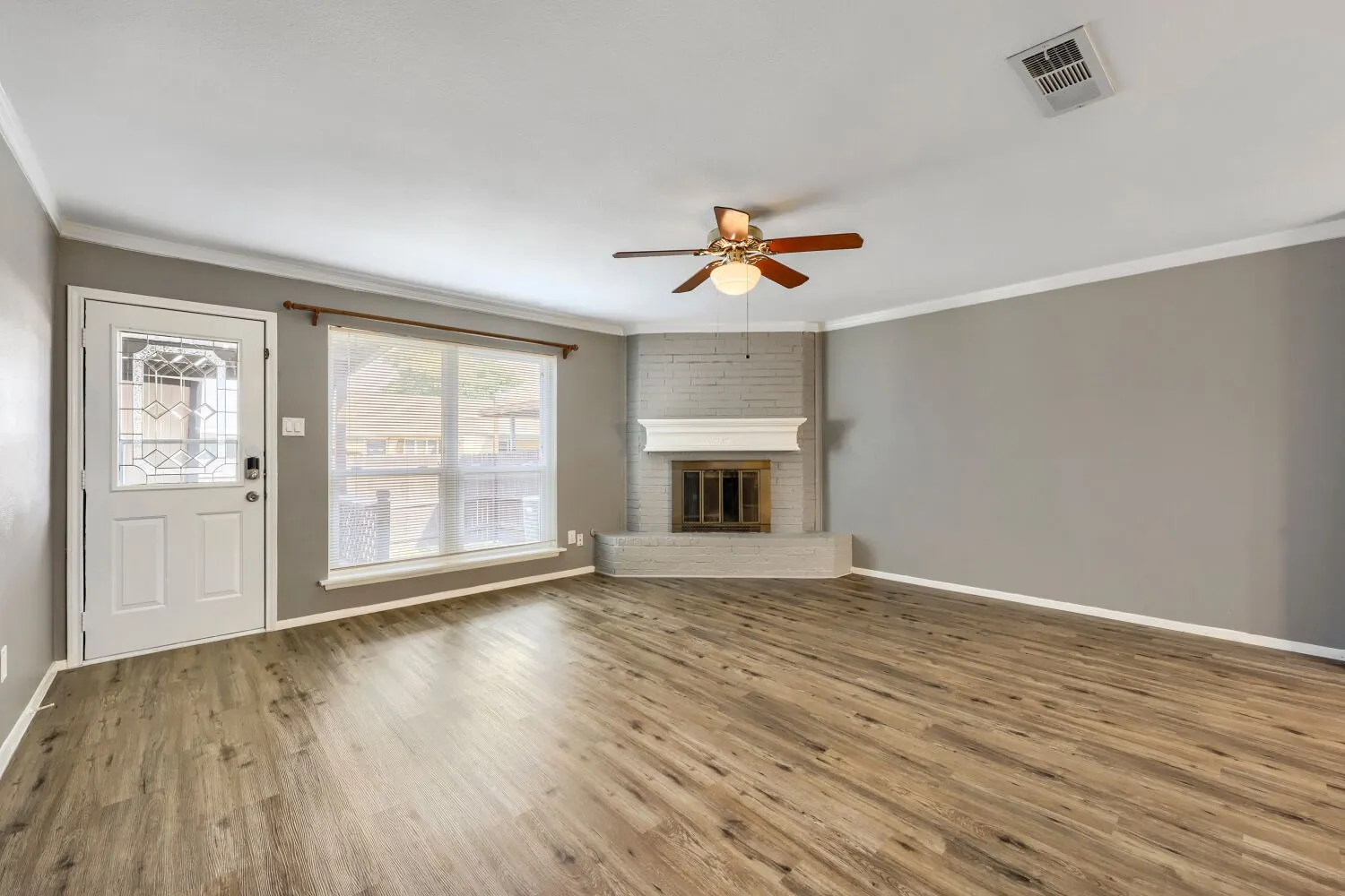 Wood-finish flooring throughout, ceiling fan, and a fireplace featuring a painted brick surround and white mantel