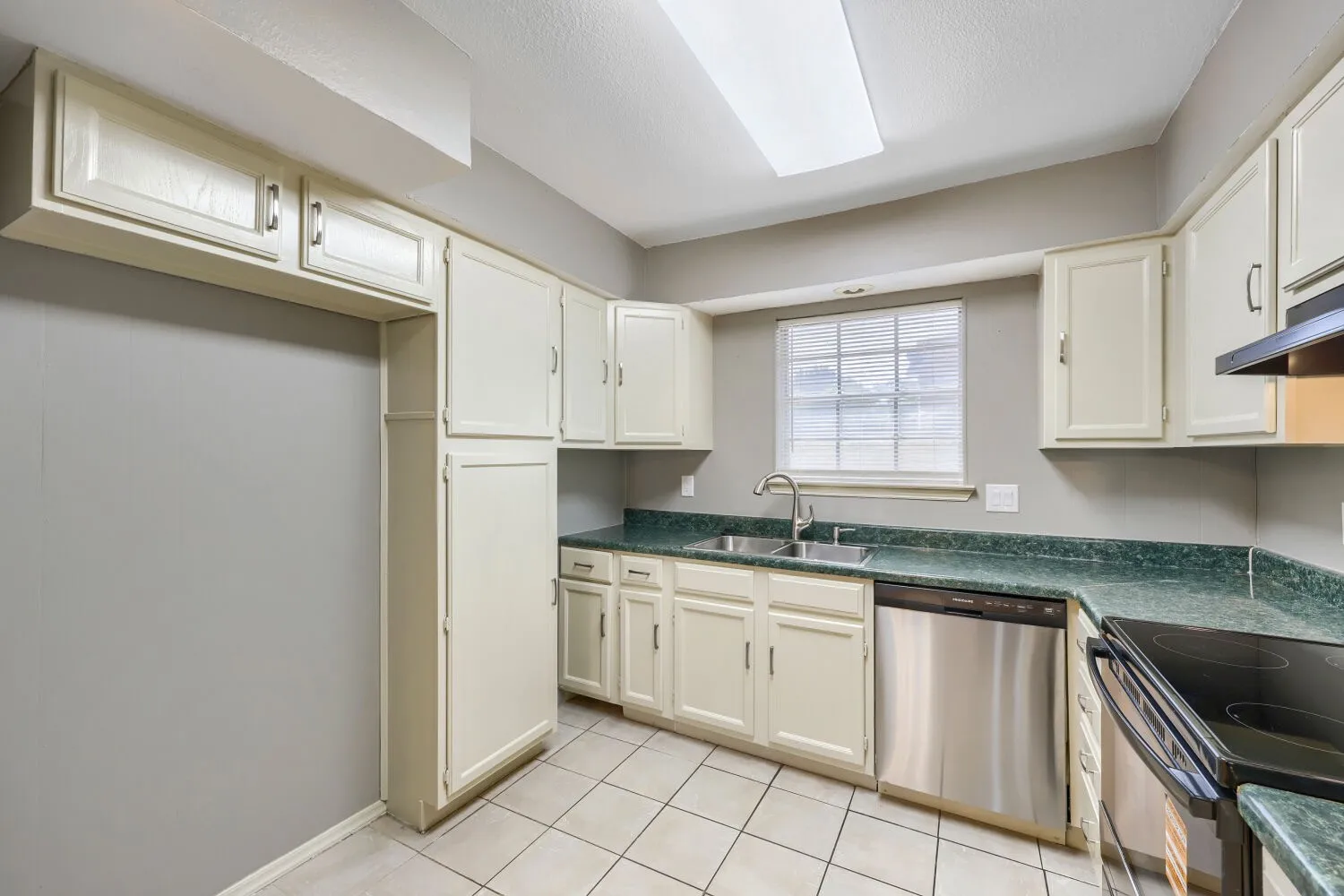 Kitchen featuring ample cabinetry, tile flooring, stainless steel dishwasher, dual basin sink, and a window for natural light