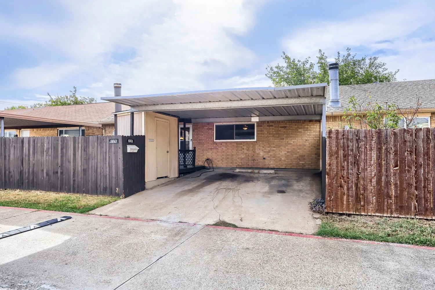 Brick exterior featuring a metal carport and wood fencing