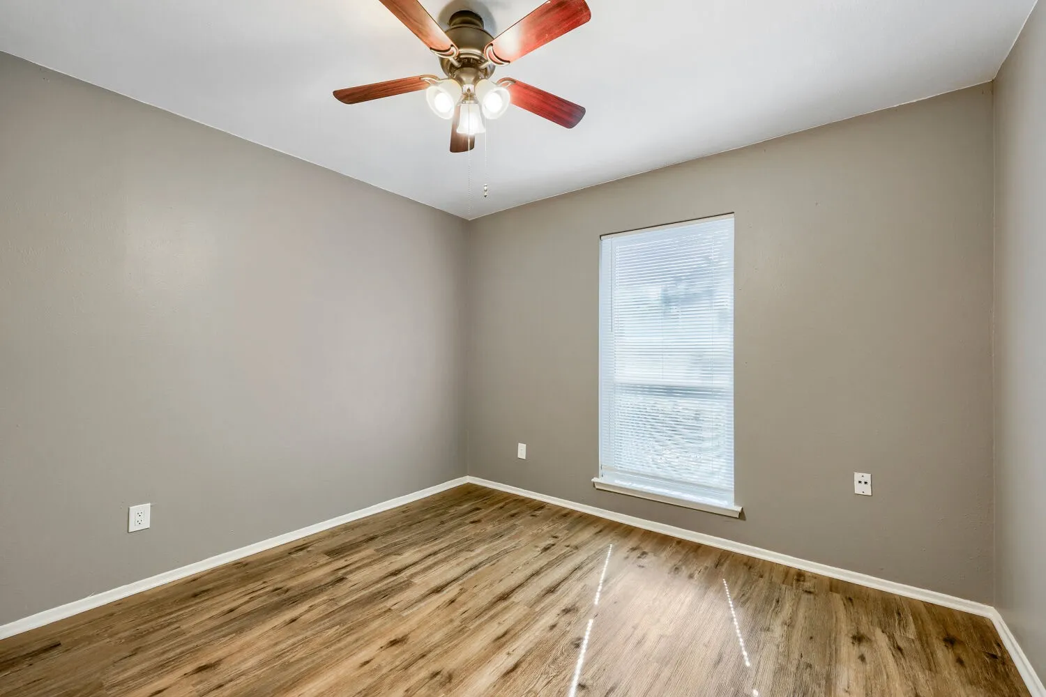 Wood-finish flooring, neutral wall tones, ceiling fan with integrated lighting, and a window with blinds