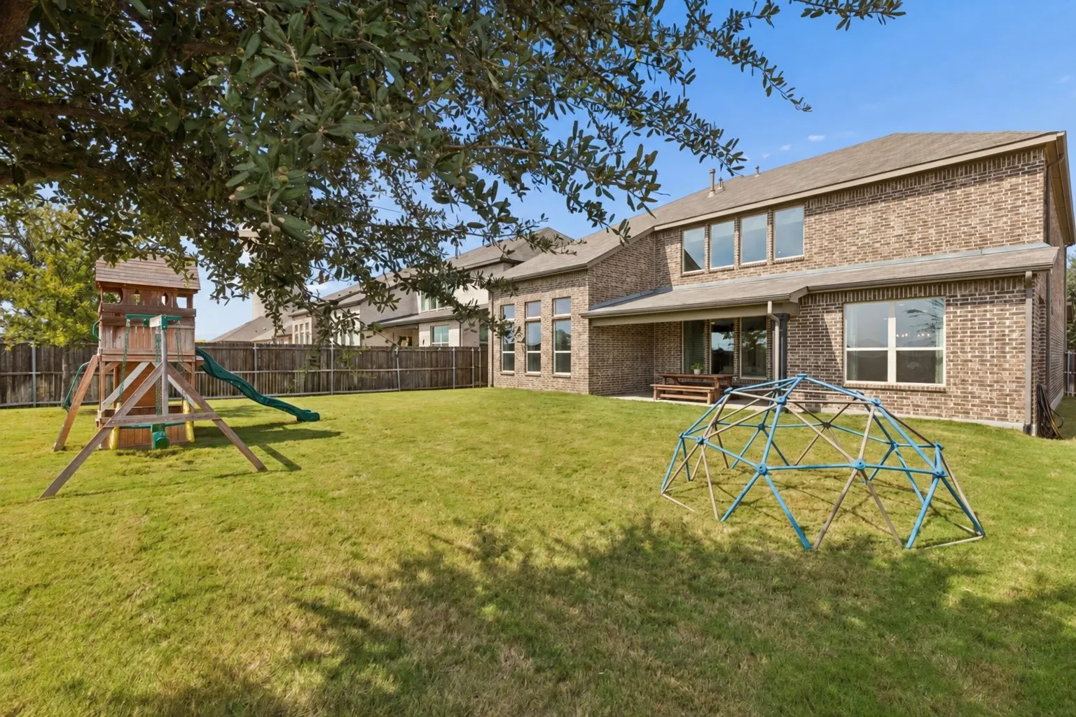 Impressive rear elevation showcases the home's handsome brick architecture, expansive windows, covered patio, and beautifully proportioned two-story design. The broad backyard provides exceptional space for recreation, entertaining, gardening, or creating a personalized outdoor retreat.